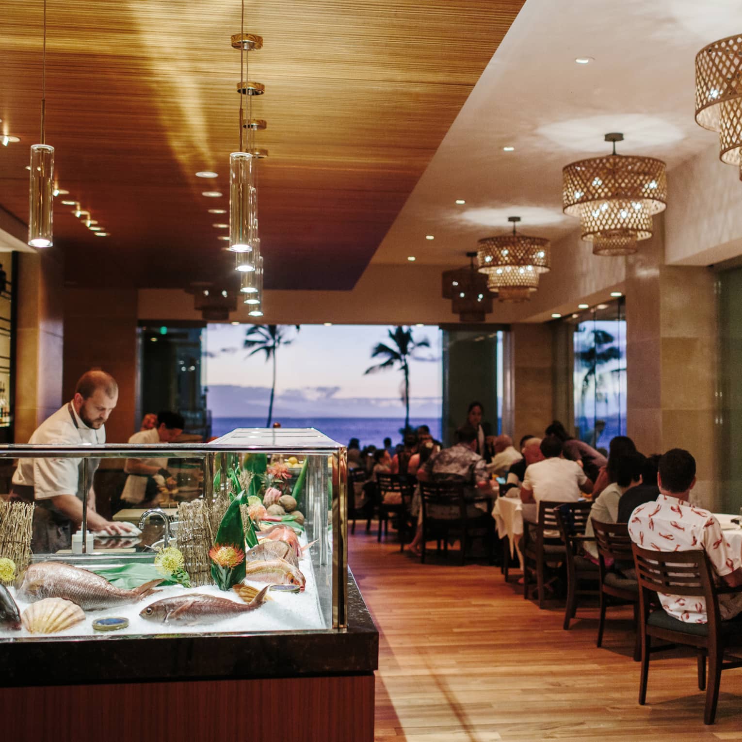 Chef prepares seafood at a sushi bar in a beachfront restaurant during sunset