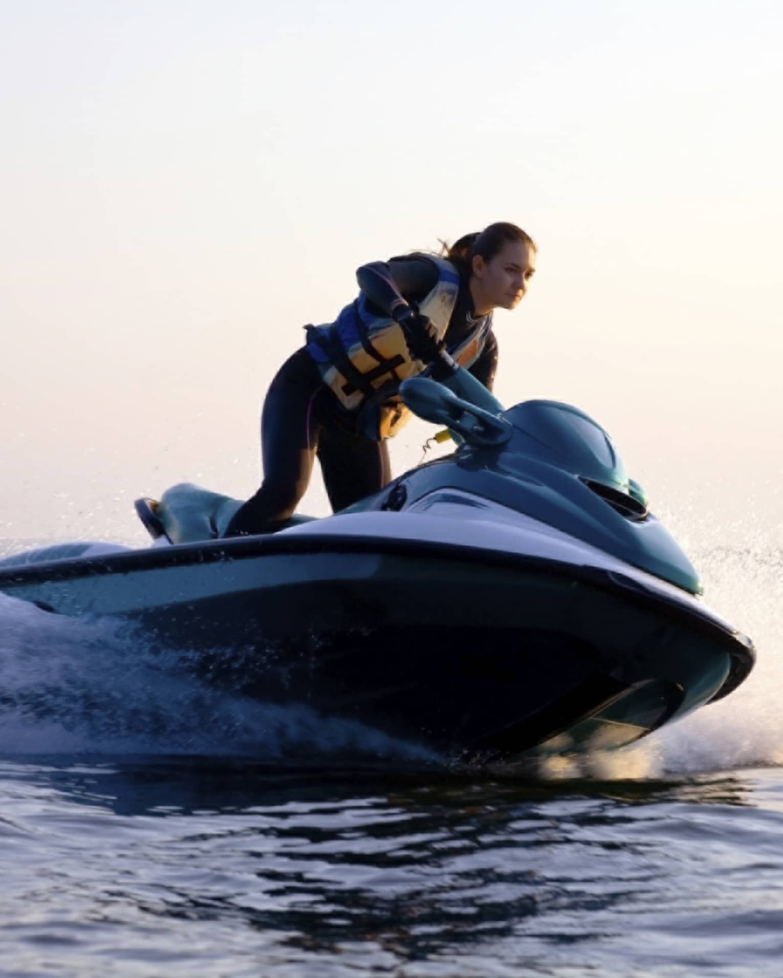 Woman wearing life jacket stands, steers jet ski on ocean at sunset