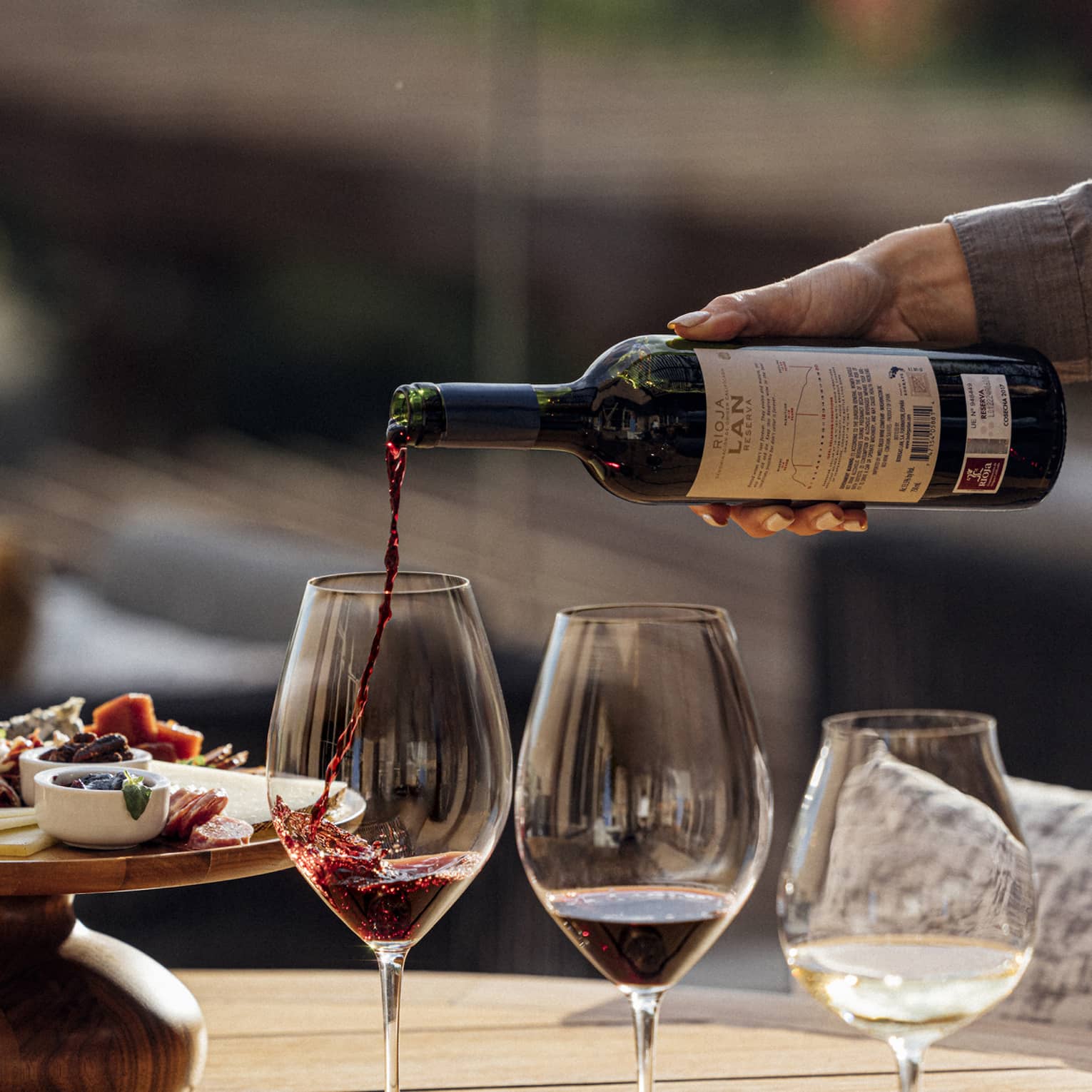 Three glasses of wine are poured next to a plate of charcuterie