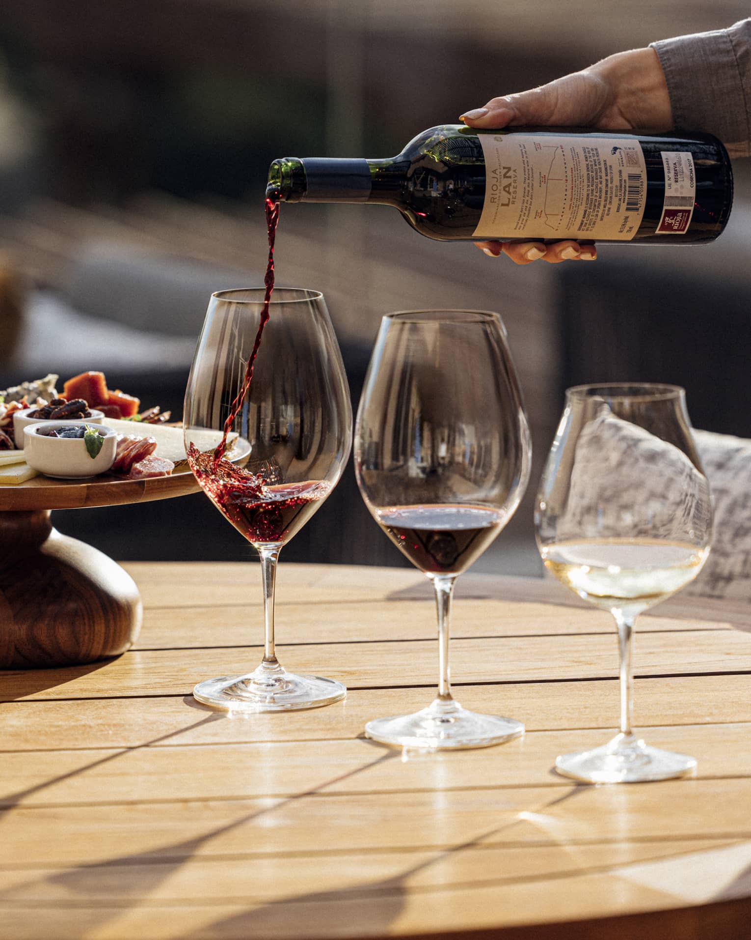 Three glasses of wine are poured next to a plate of charcuterie