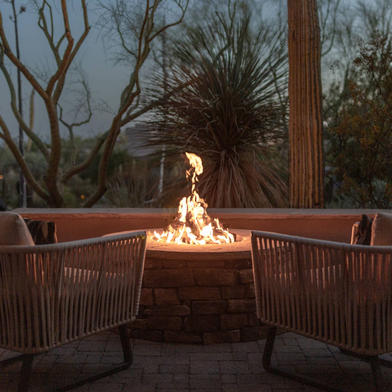 Two empty patio chairs in front of a lit fire pit in the evening