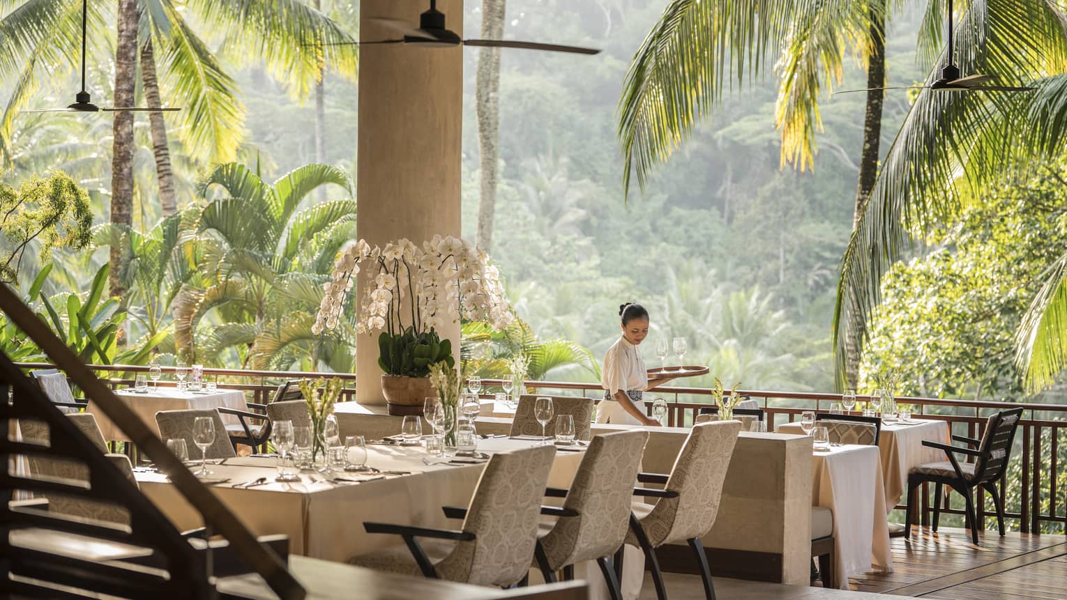 Person sets table on veranda at luxury resort restaurant by forest