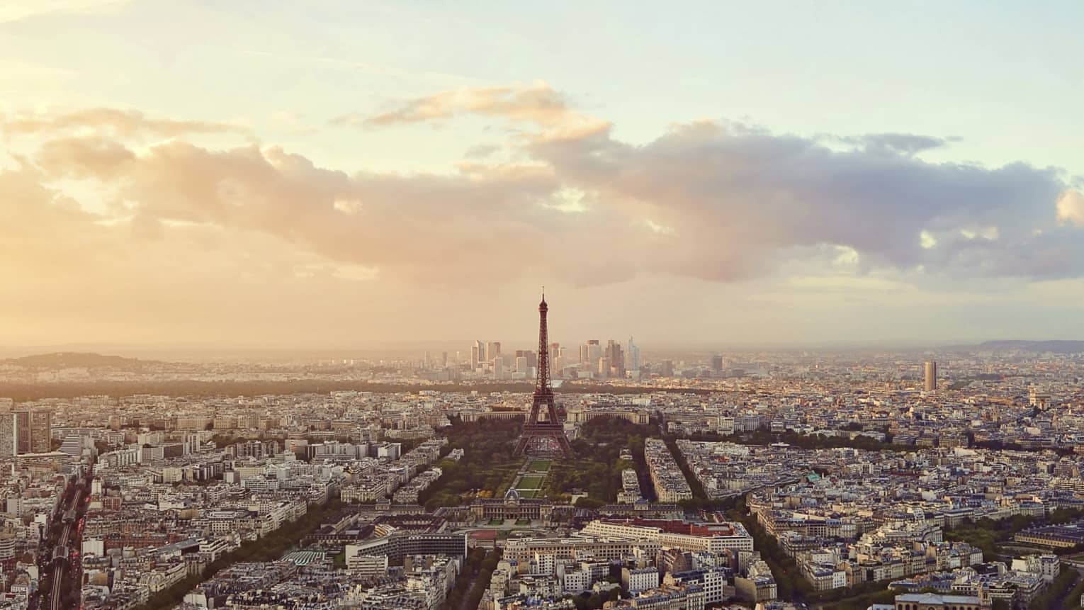 Sweeping city view of Paris rooftops, buildings, Eiffel tower at sunset