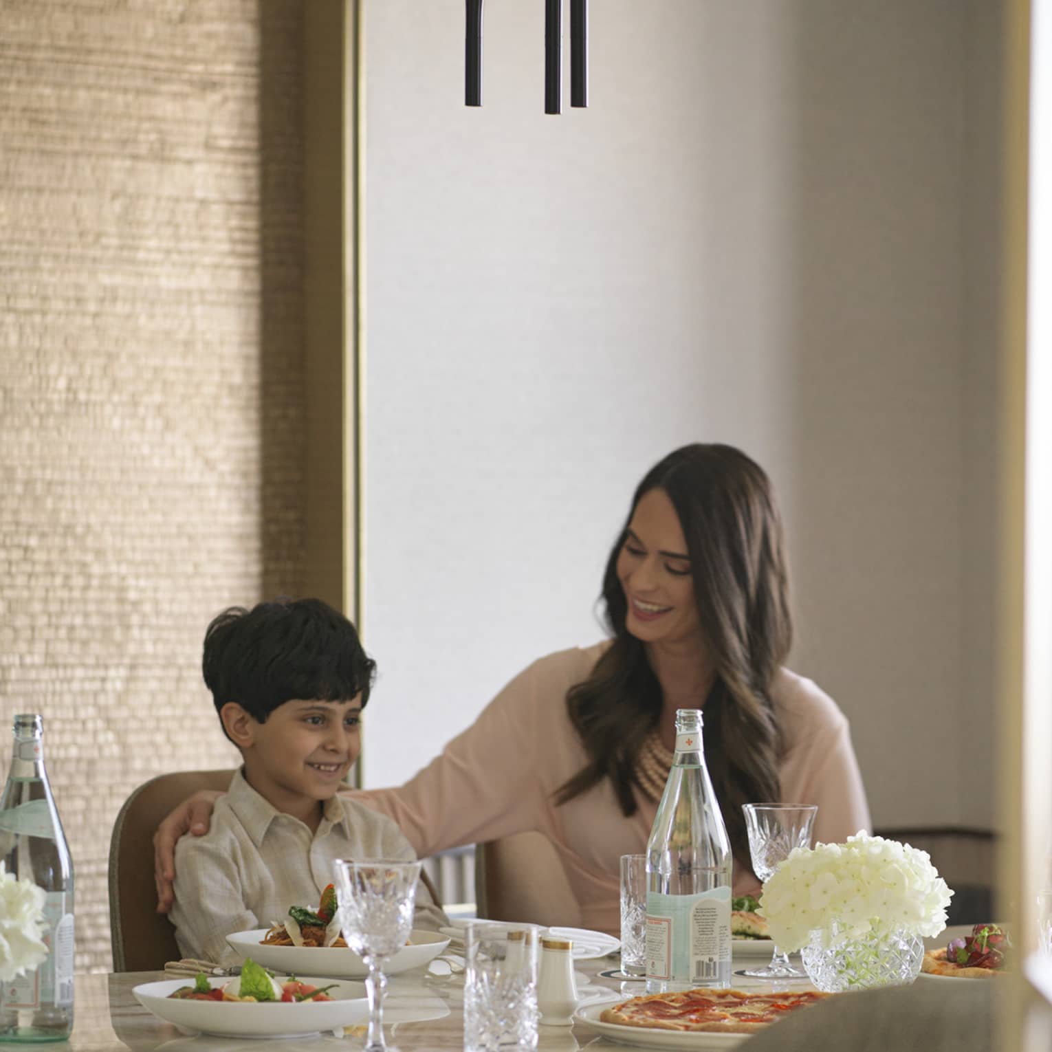 A view from the doorway of a smiling family sitting around a nicely set table with an assortment of food placed before them.