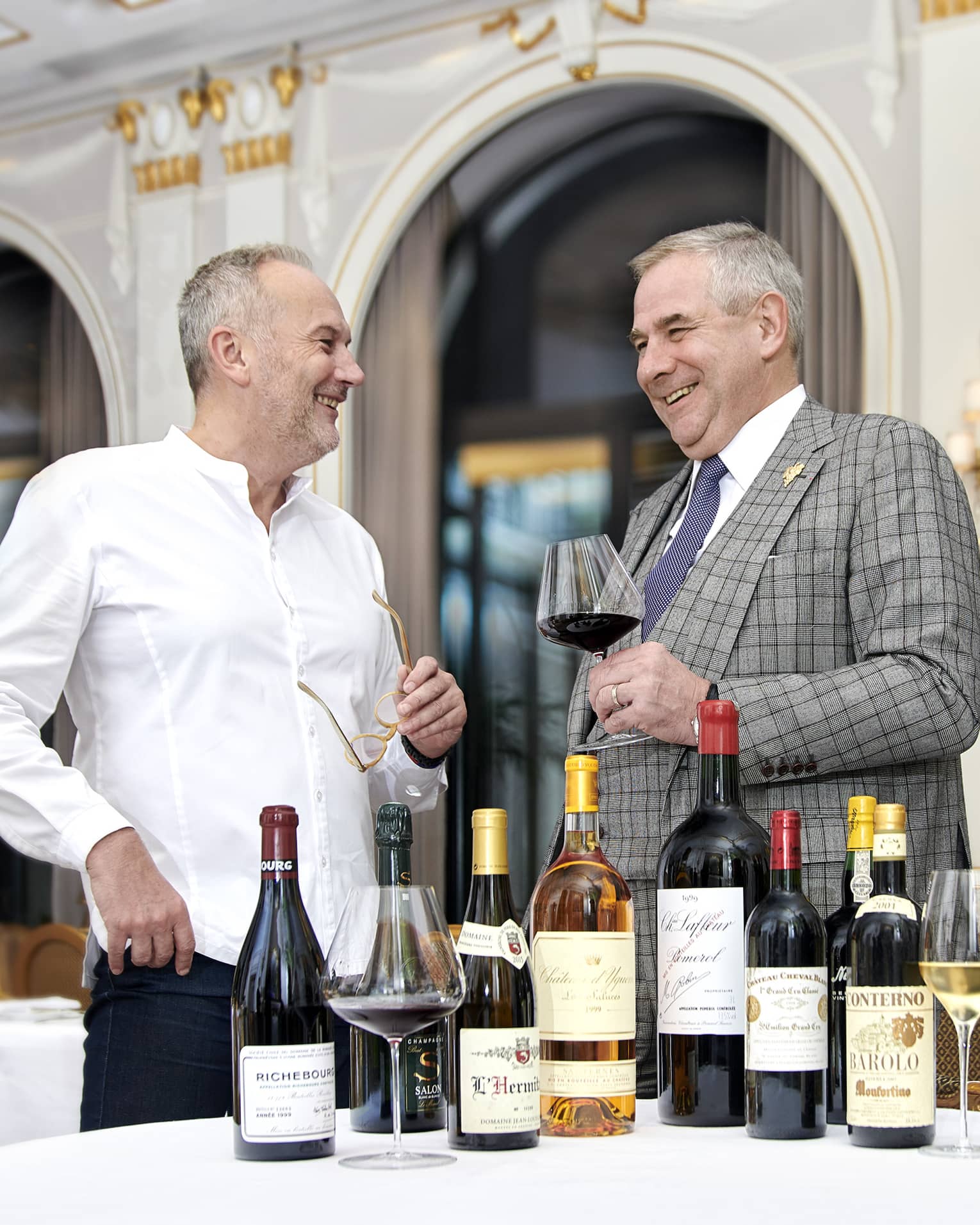 Chef Christian Le Squer and sommelier Eric Beaumard standing, smiling with wine in had and wine bottles on table
