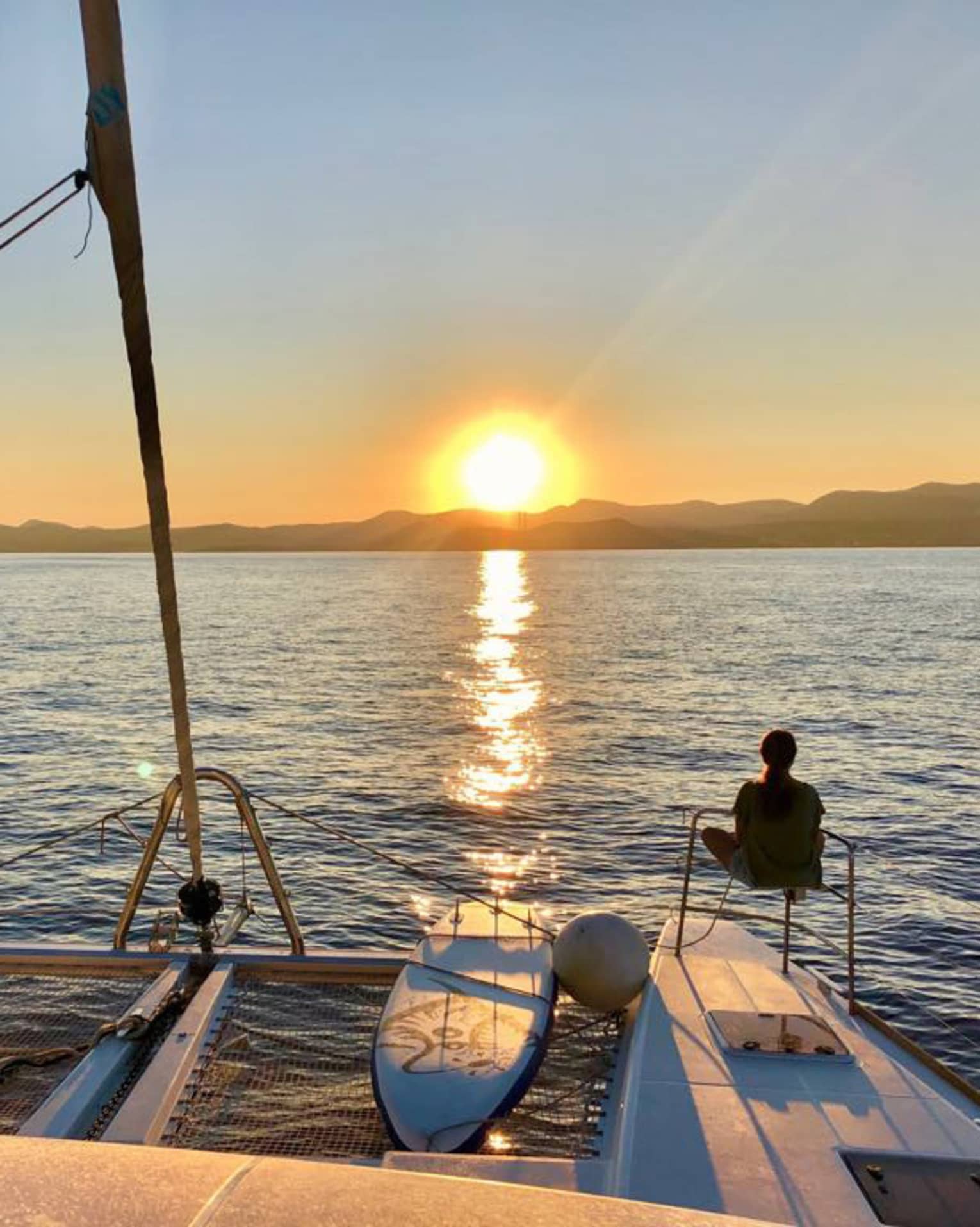 Two guests lounge on luxury sailboat near stern railing at sunset