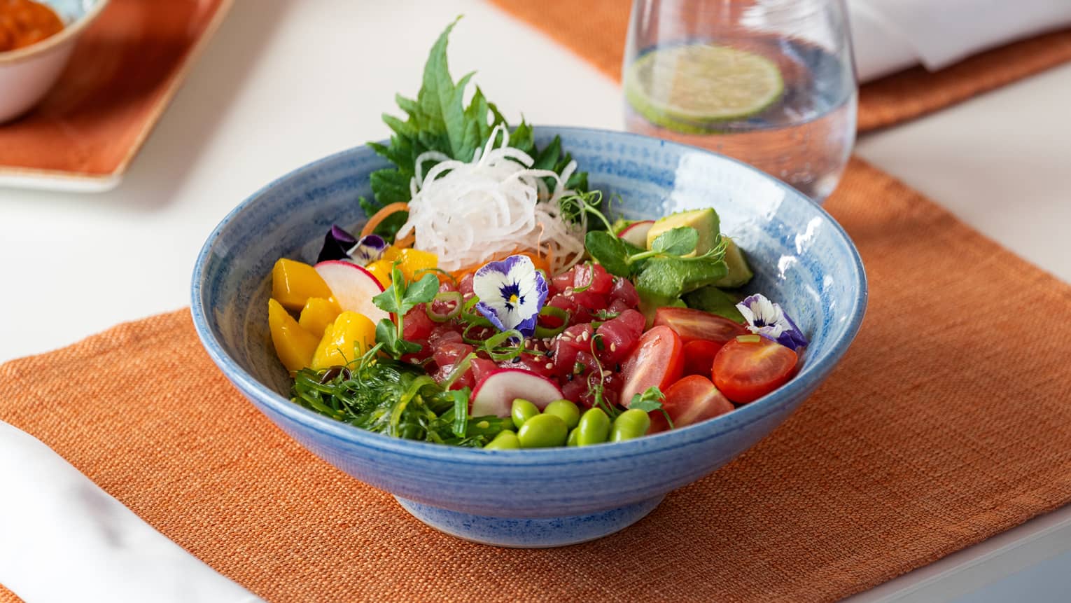 Poke bowl with sushi rice, avocado, mango, edamame, cherry tomatoes, wakame and carrots served in a blue bowl
