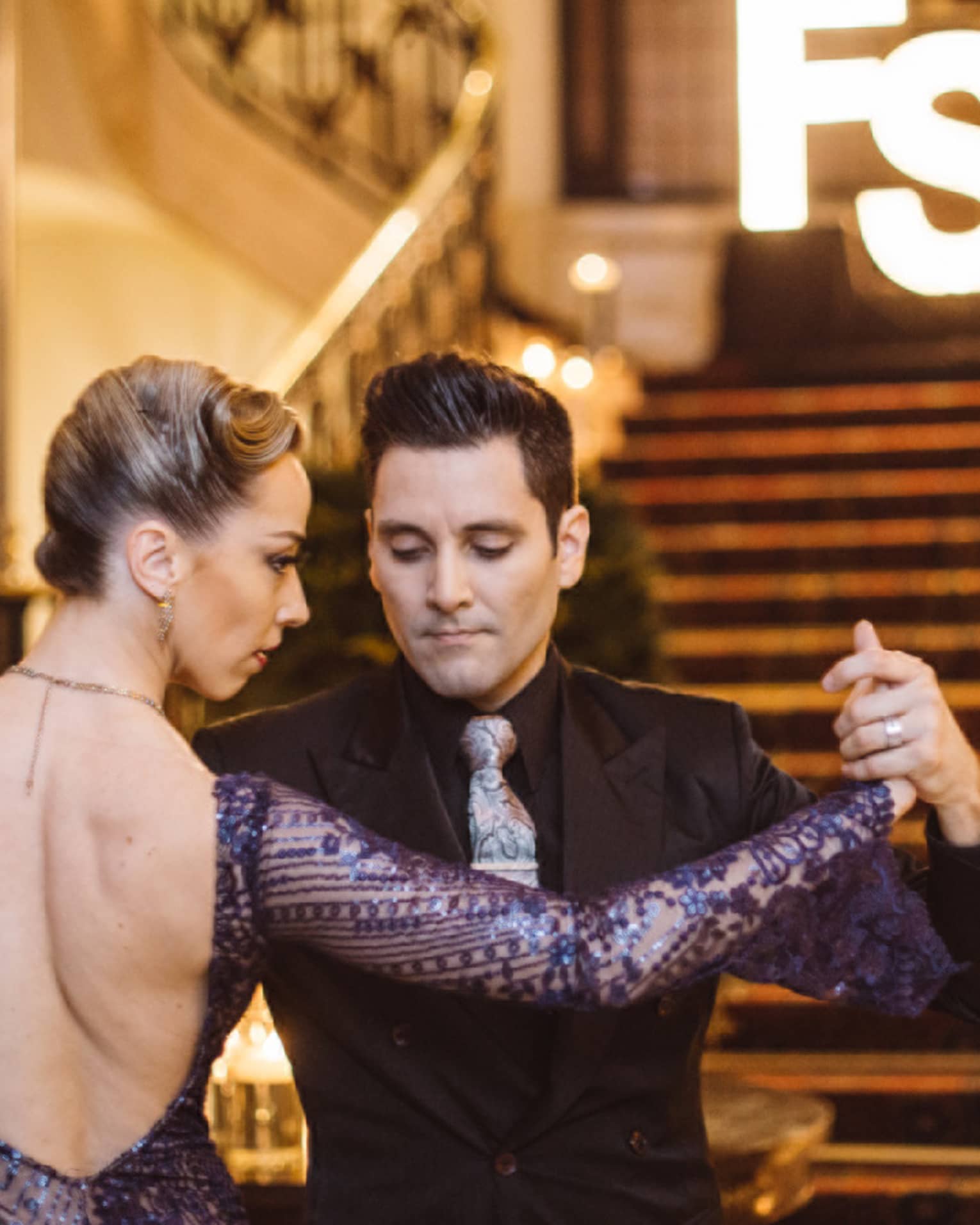 A man and woman tango dancing at the bottom of a wide red carpeting stairway