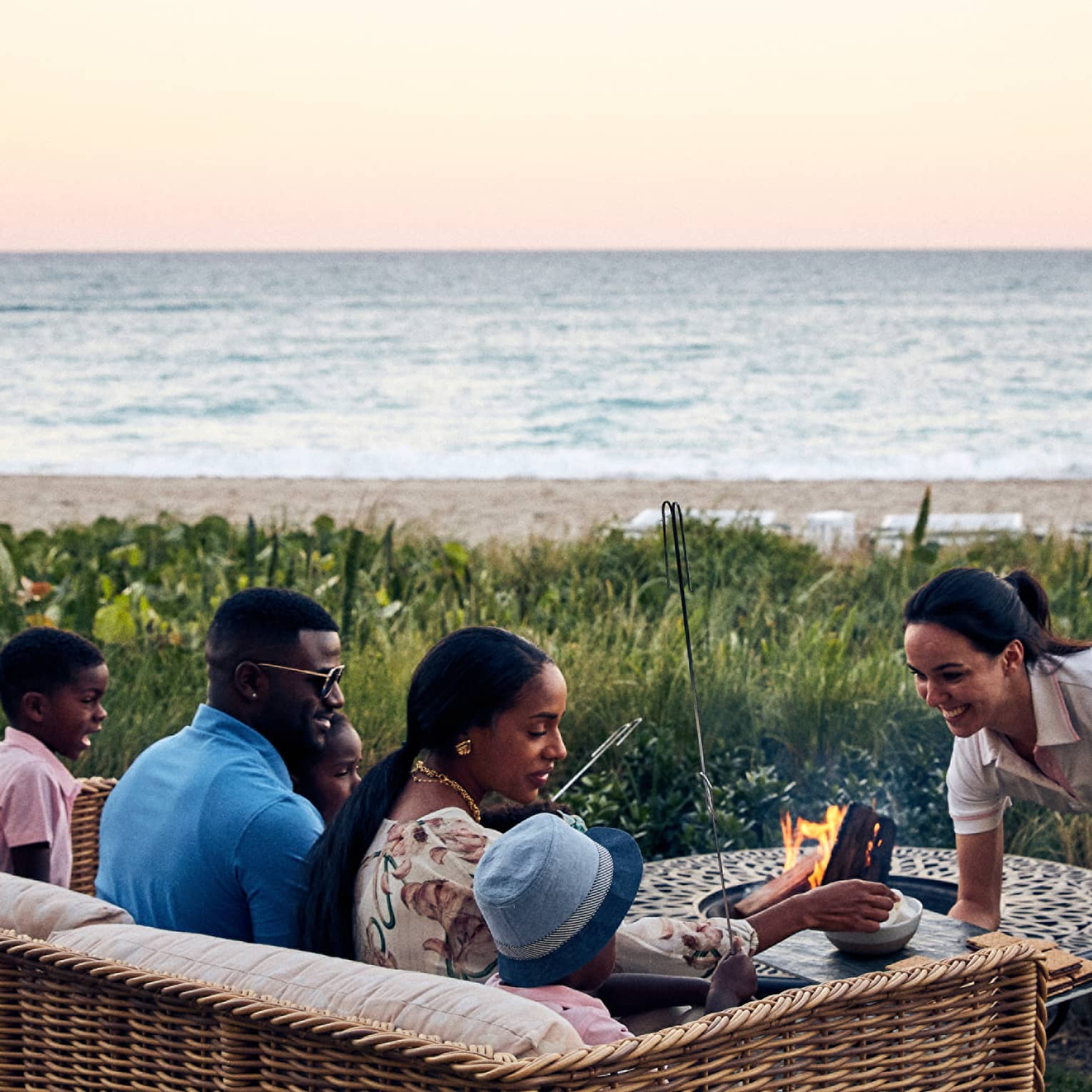 A family with a husband, wife, and two children talking to a staff member while the cook s'mores outside near water.