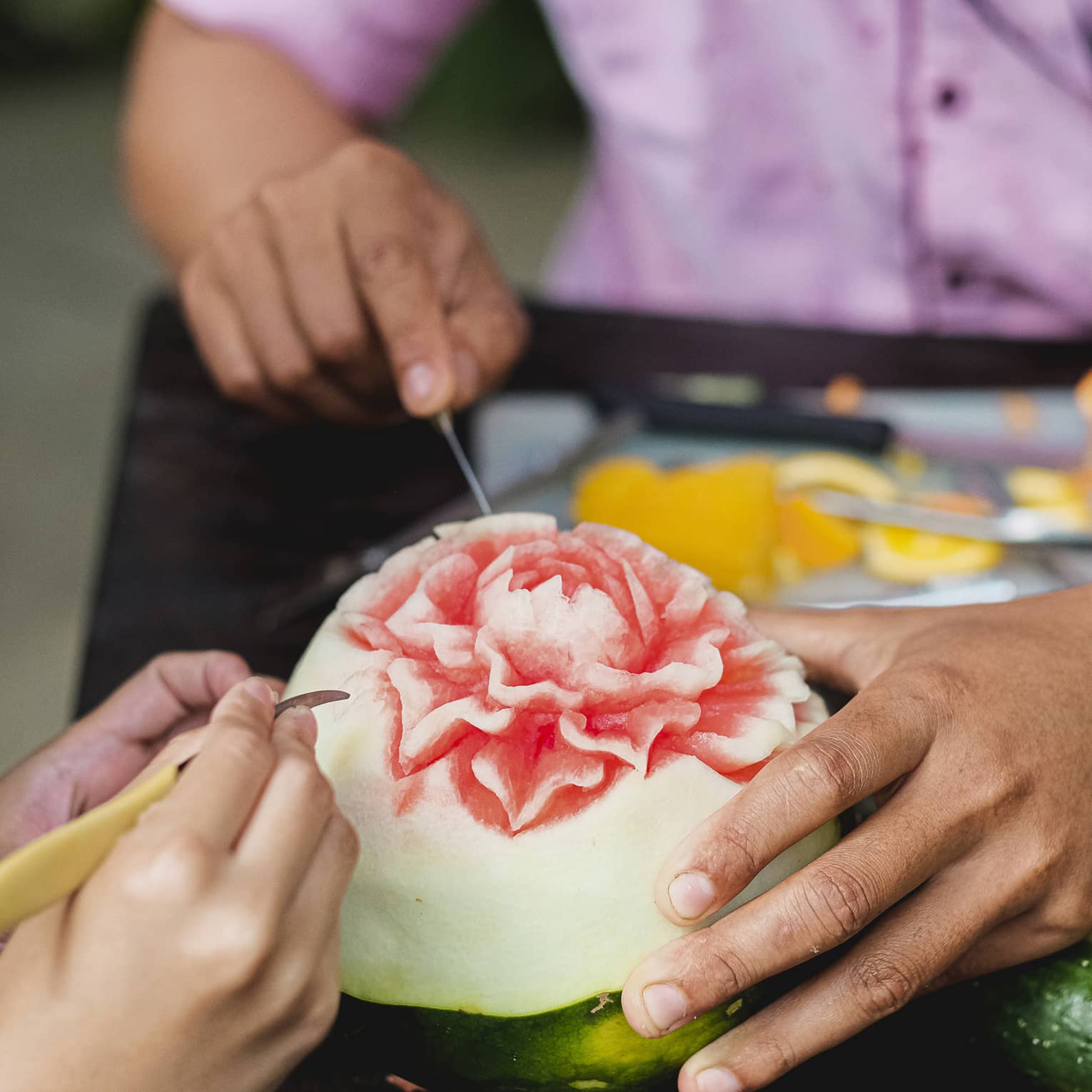 Close-up shot of man and child's hands carving intricate flower into watermelon