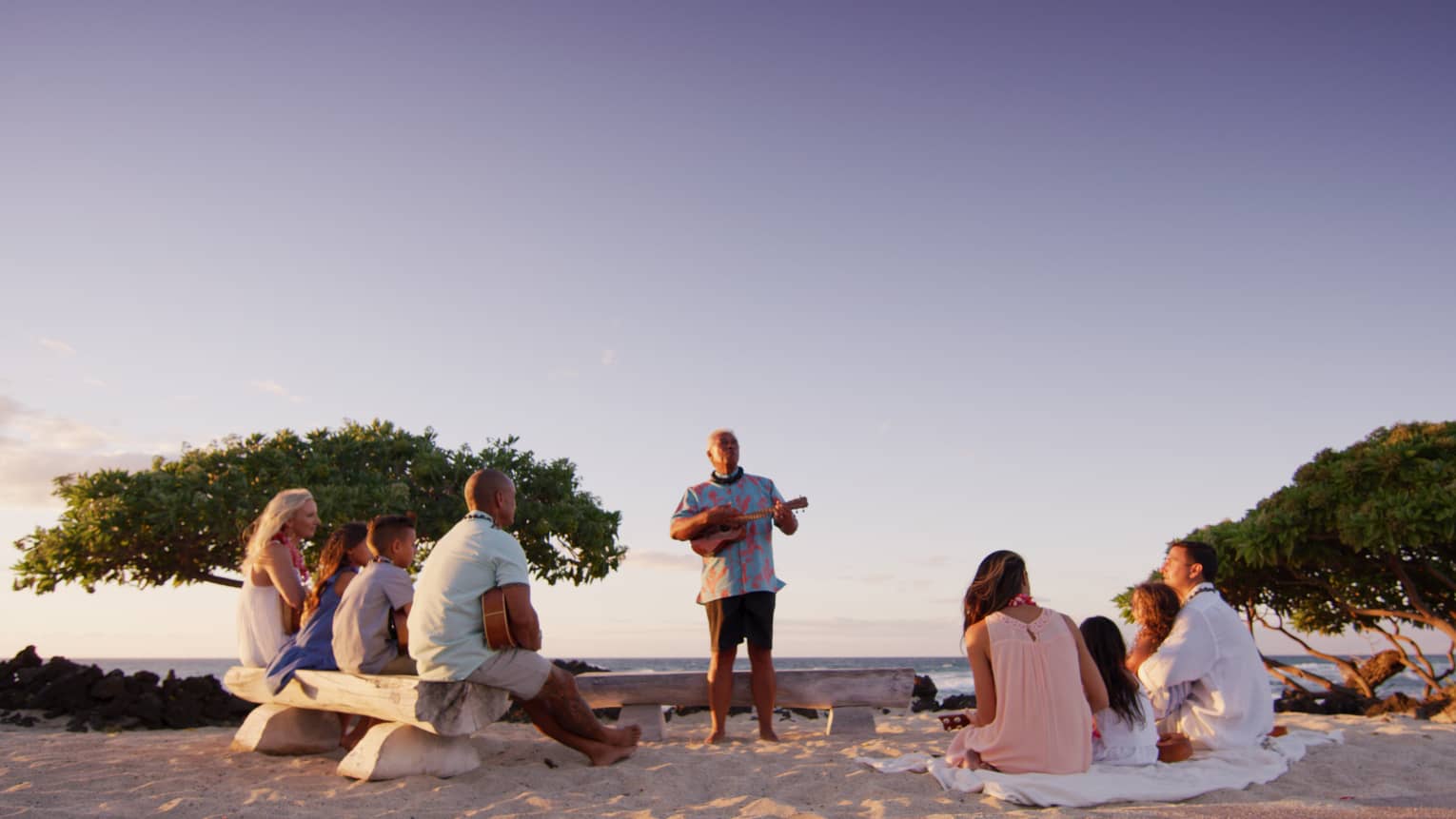 Man plays ukulele for families sitting on beach