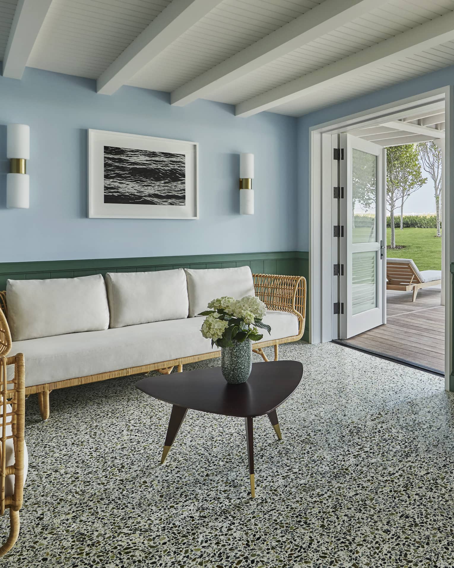White-cushioned rattan furniture in a spacious living room of a private cabana, with double doors opening onto a scenic deck.