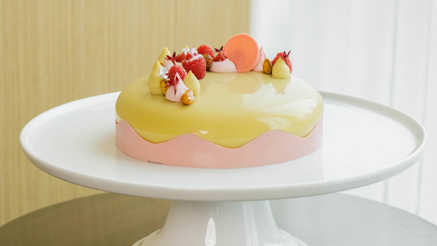 Round cake with a glazed pistachio-colored icing, a pink scalloped-edge border around the side and a candied-fruit topping is set atop a round white cake stand