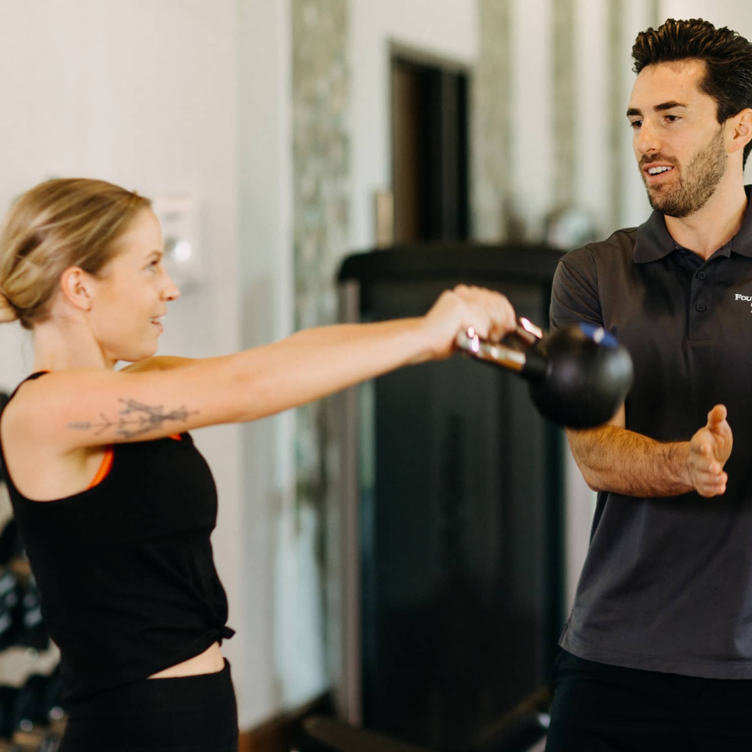 Male fitness trainer works with female guest who is using a kettlebell