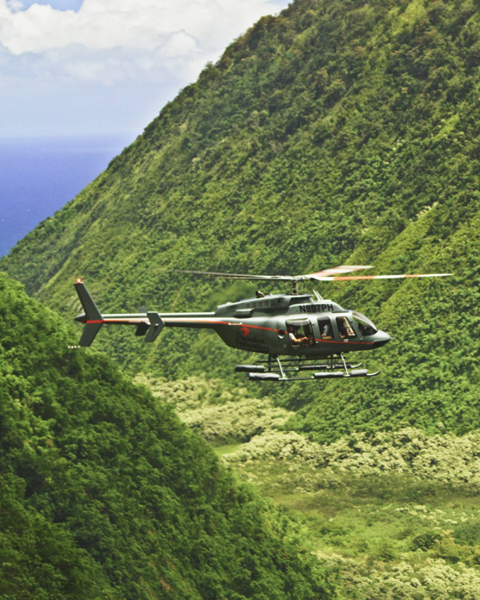 Orange and grey helicopter flying through crevice between green mountains