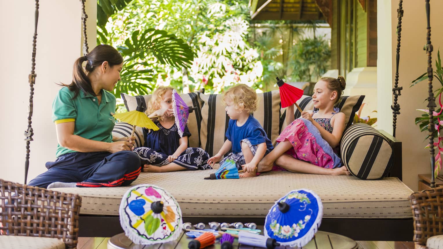 Hotel staff relaxes with children, hold colourful paper umbrellas on large hanging patio bed