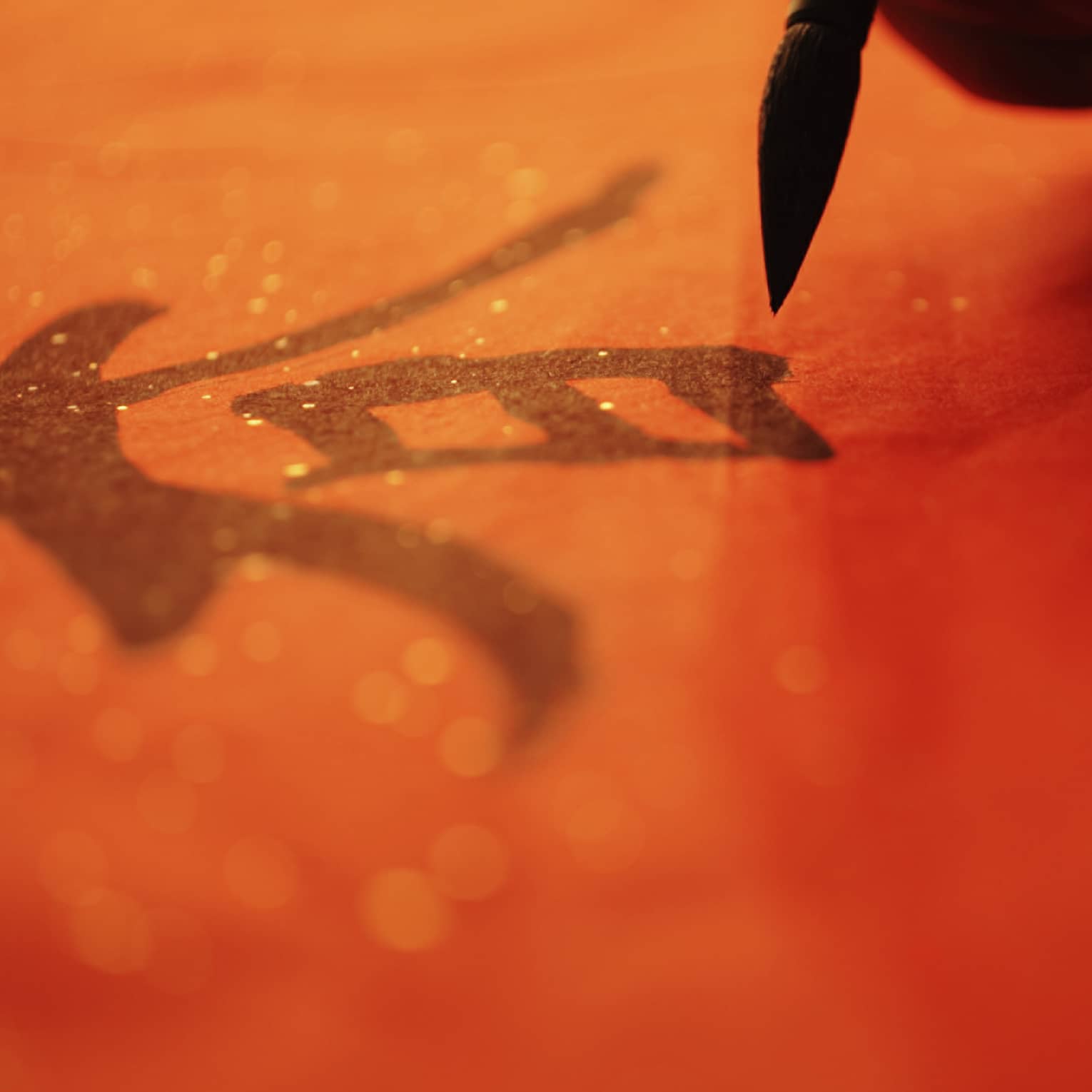 Close up of a hand painting a Chinese graphic on a red background 