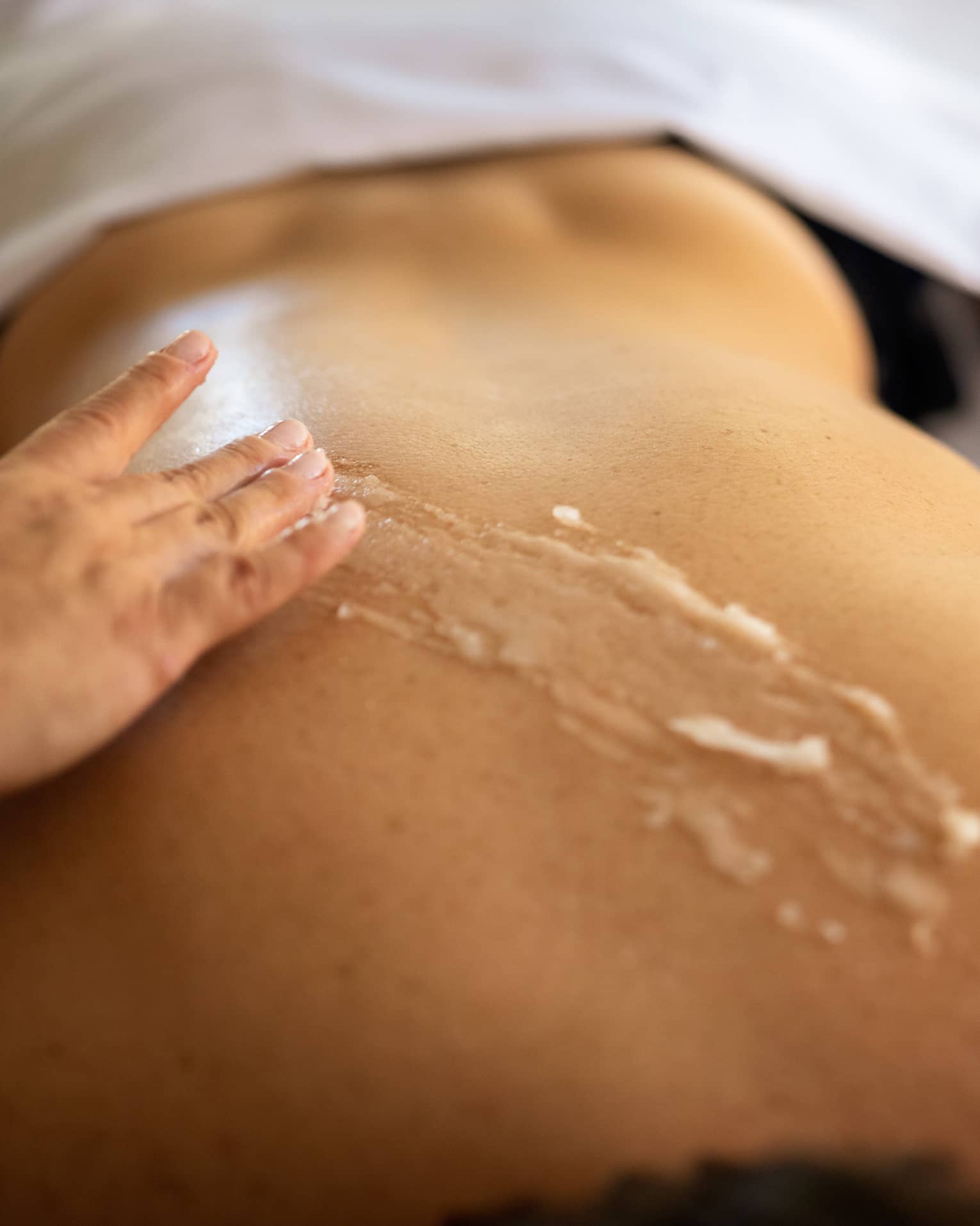 A therapist applies scrub to a person's back during spa treatment