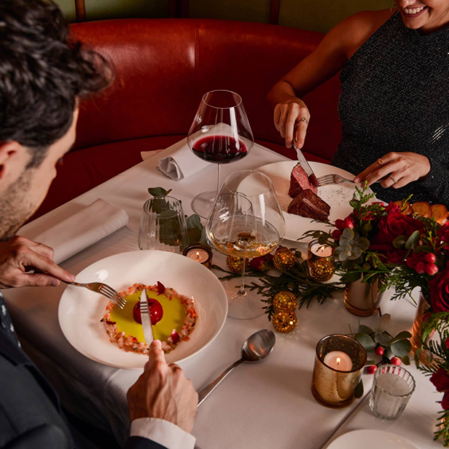 Two guests sitting at a dining table holding silverware to eat their food.