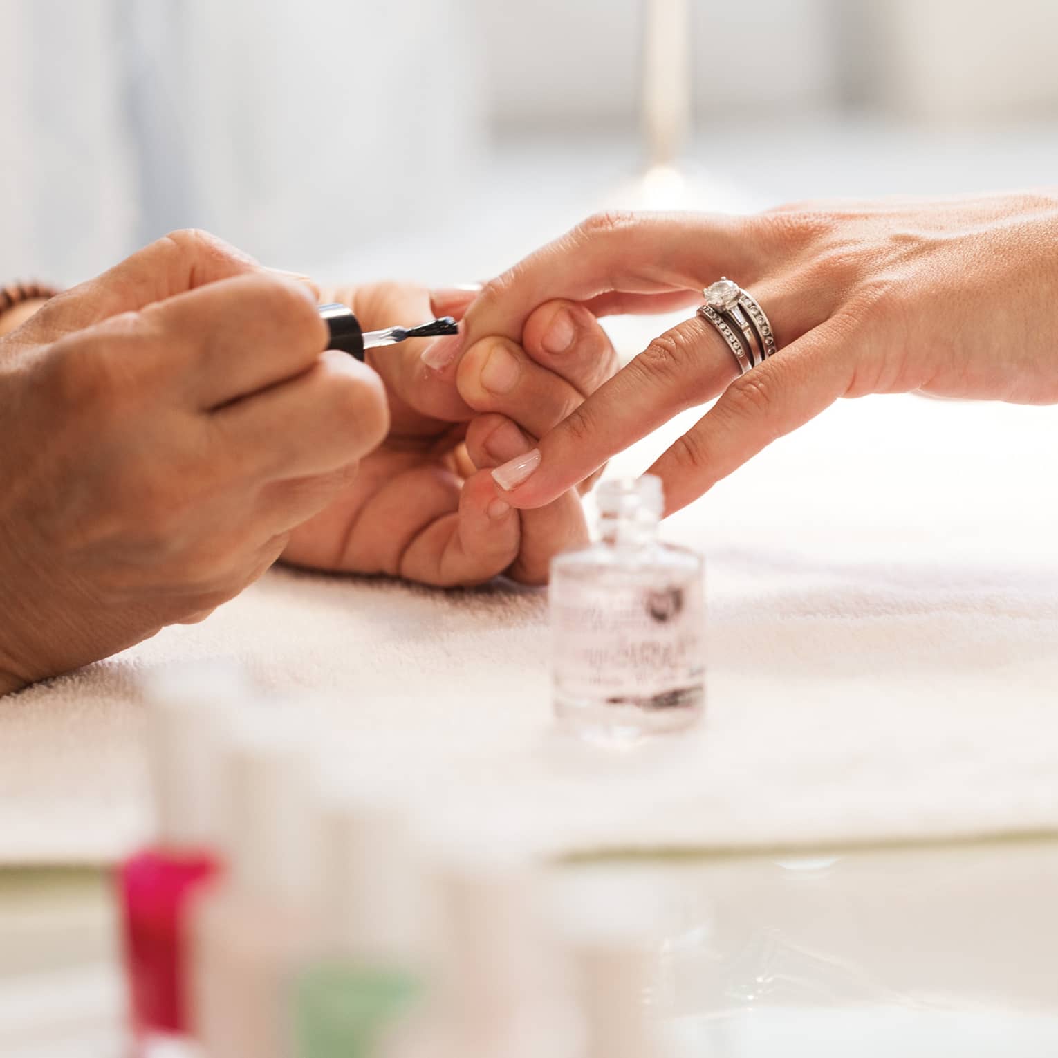 Close-up of woman in white robe getting clear polish manicure at spa table