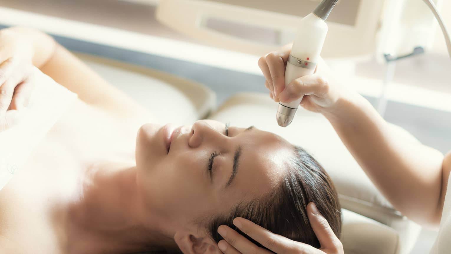 An aesthetician uses a tool on the face of a relaxing woman.