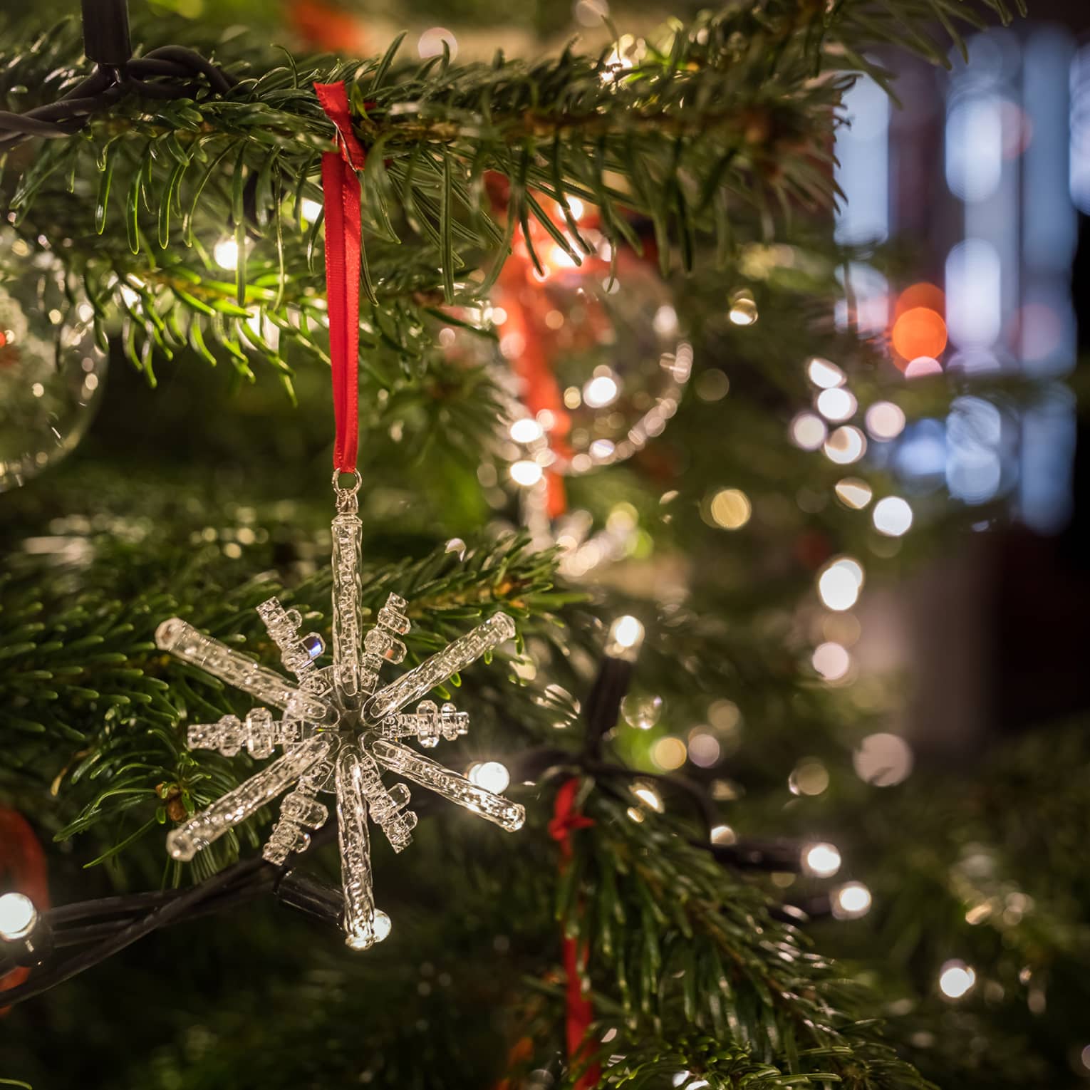 Close-up of a crystal snowflake ornament hanging on a Christmas tree with festive lights in the background