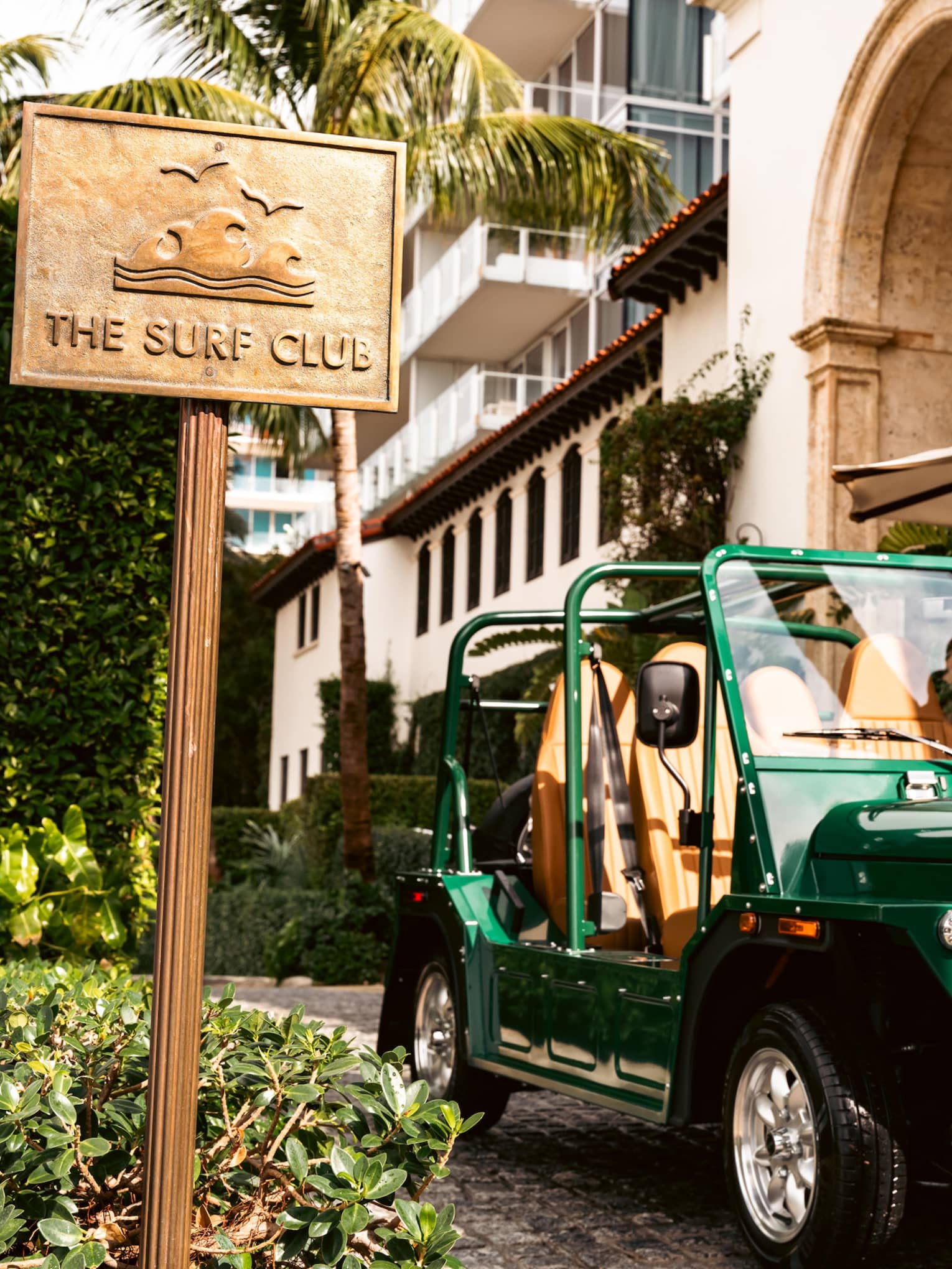 Green MOKE car parked outside of the building next to "The Surf Club" sign.