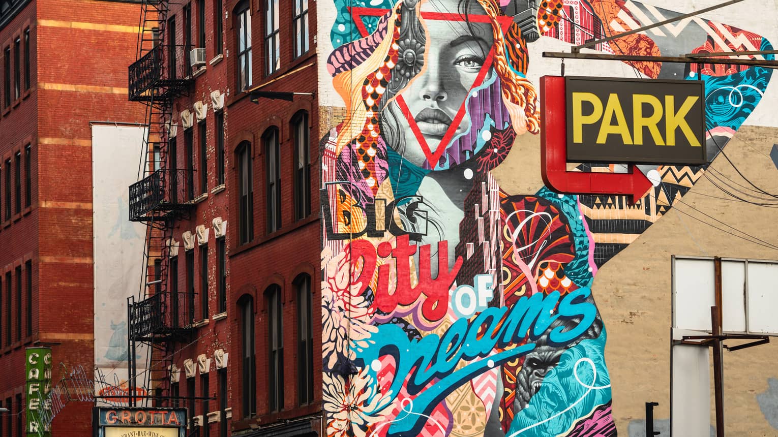 A painted mural of a grey face and a colourful arm on the side of a red brick building.