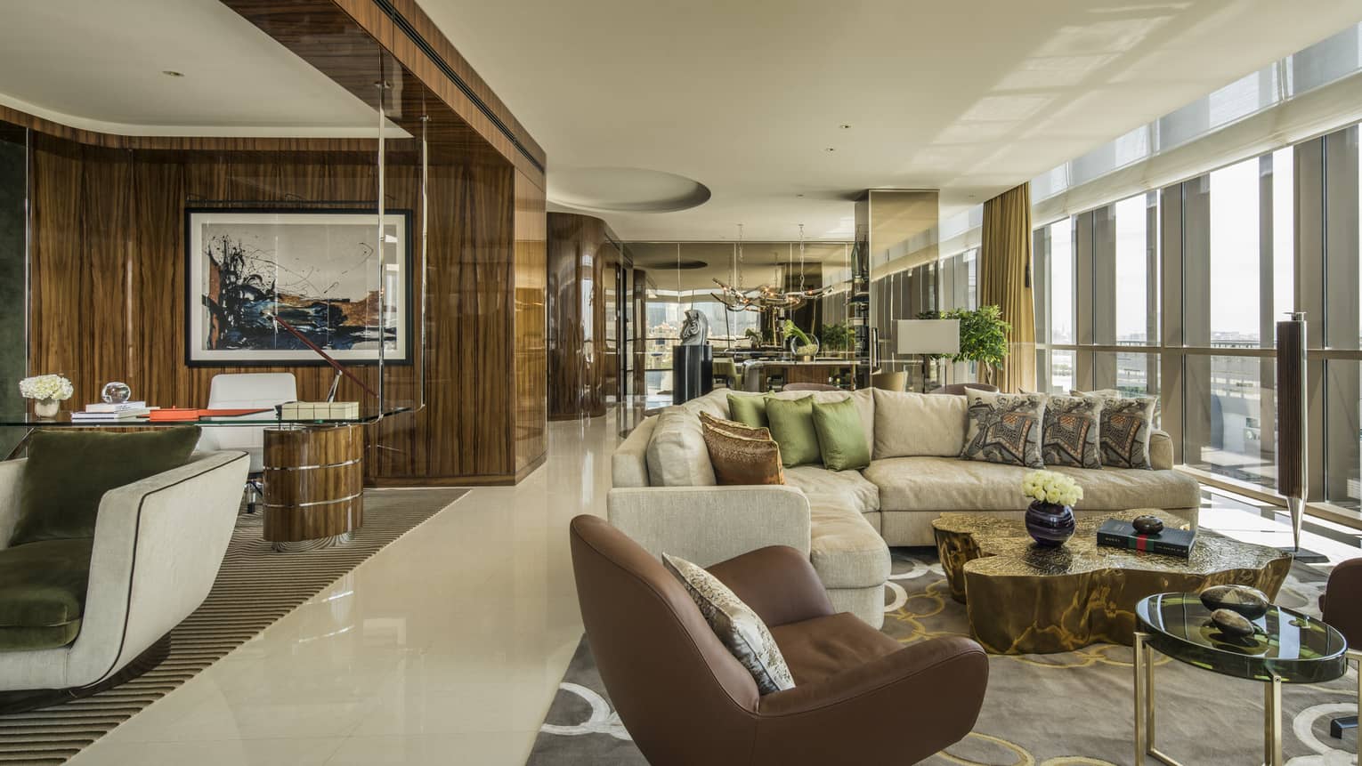 Penthouse Suite with large L-shaped beige sofa with pillows, leather armchairs, floor-to-ceiling windows along wall