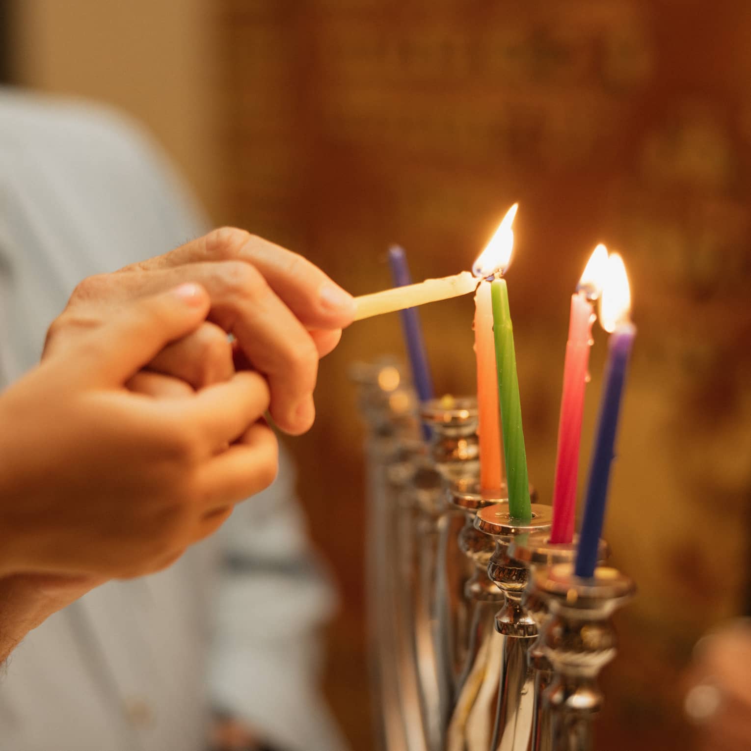 Two hands light multi-coloured candles on a menorah