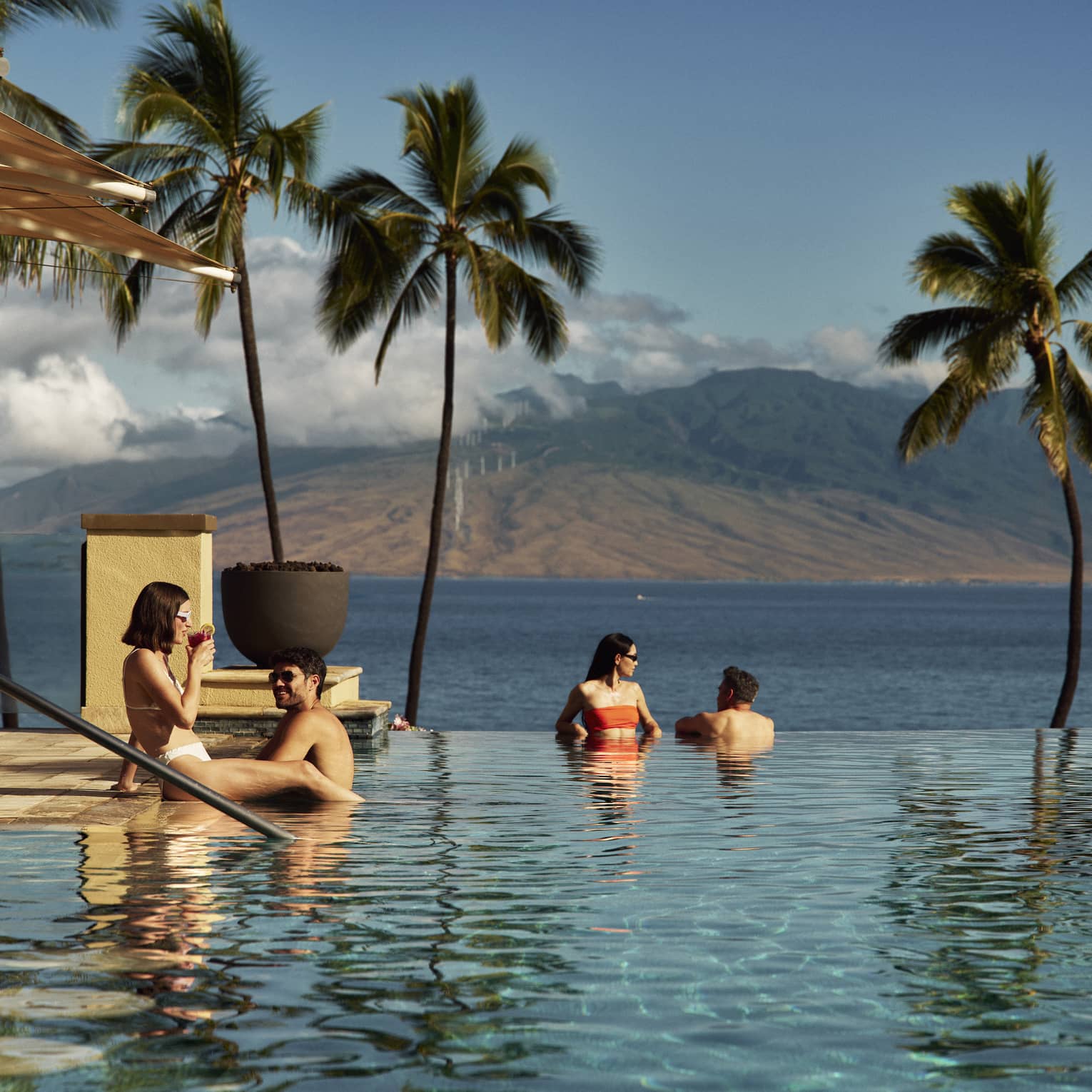 People relaxing in an infinity pool, enjoying ocean and mountain views at a Four Seasons luxury resort