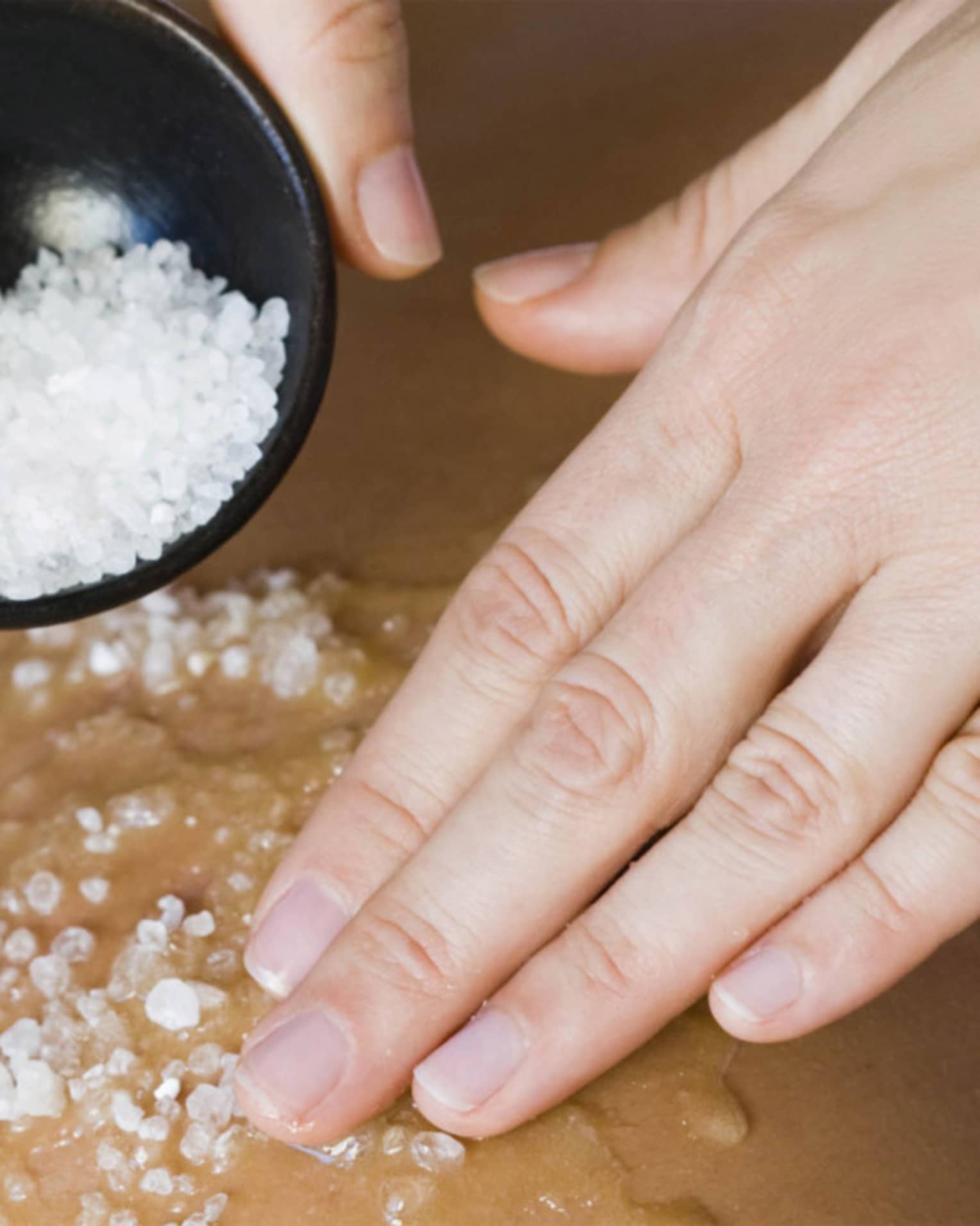 Close-up of large spa salts in bowl, hand rubbing crystals on bare back
