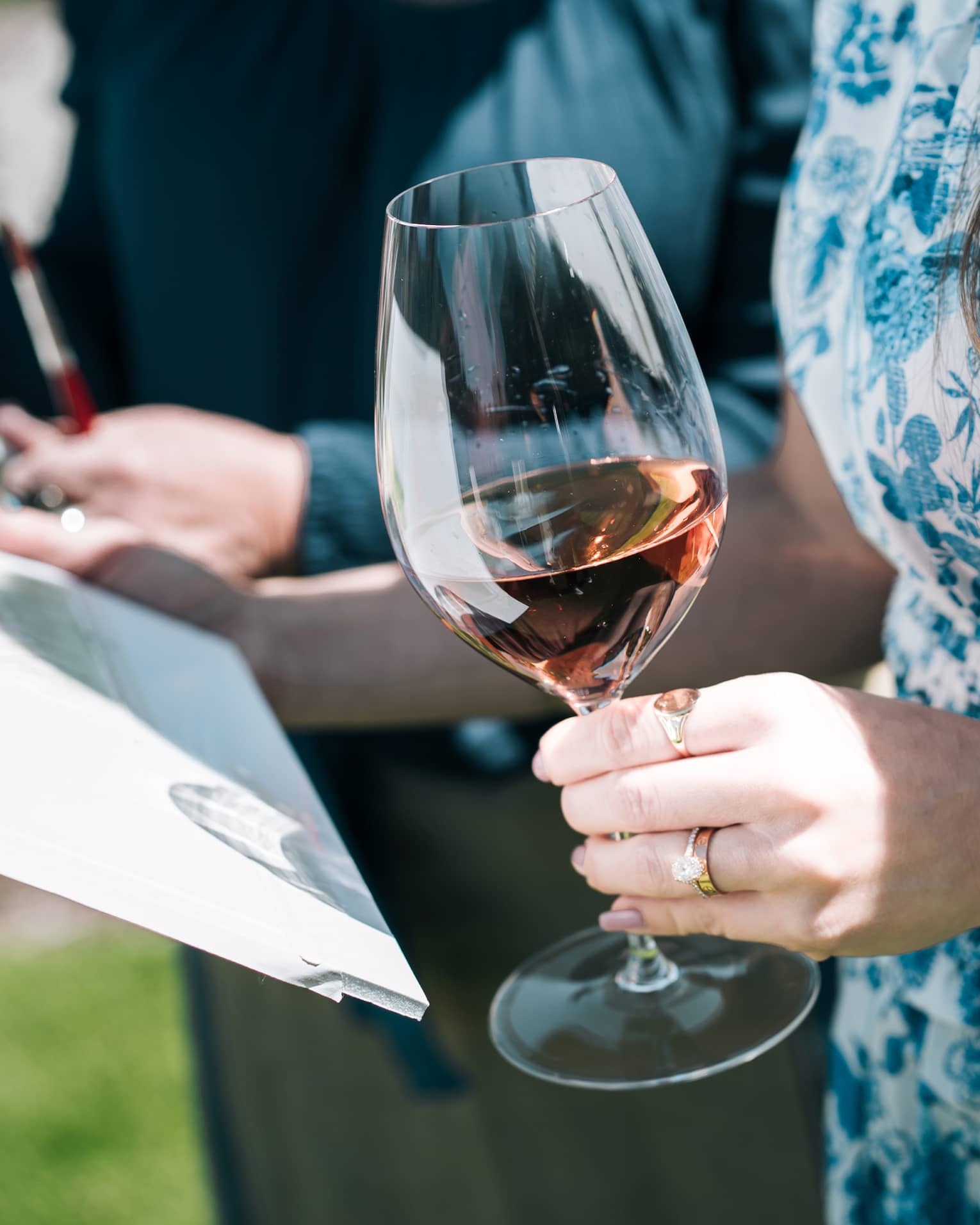 Person holds a glass of wine in one hand while holding a painting in the other