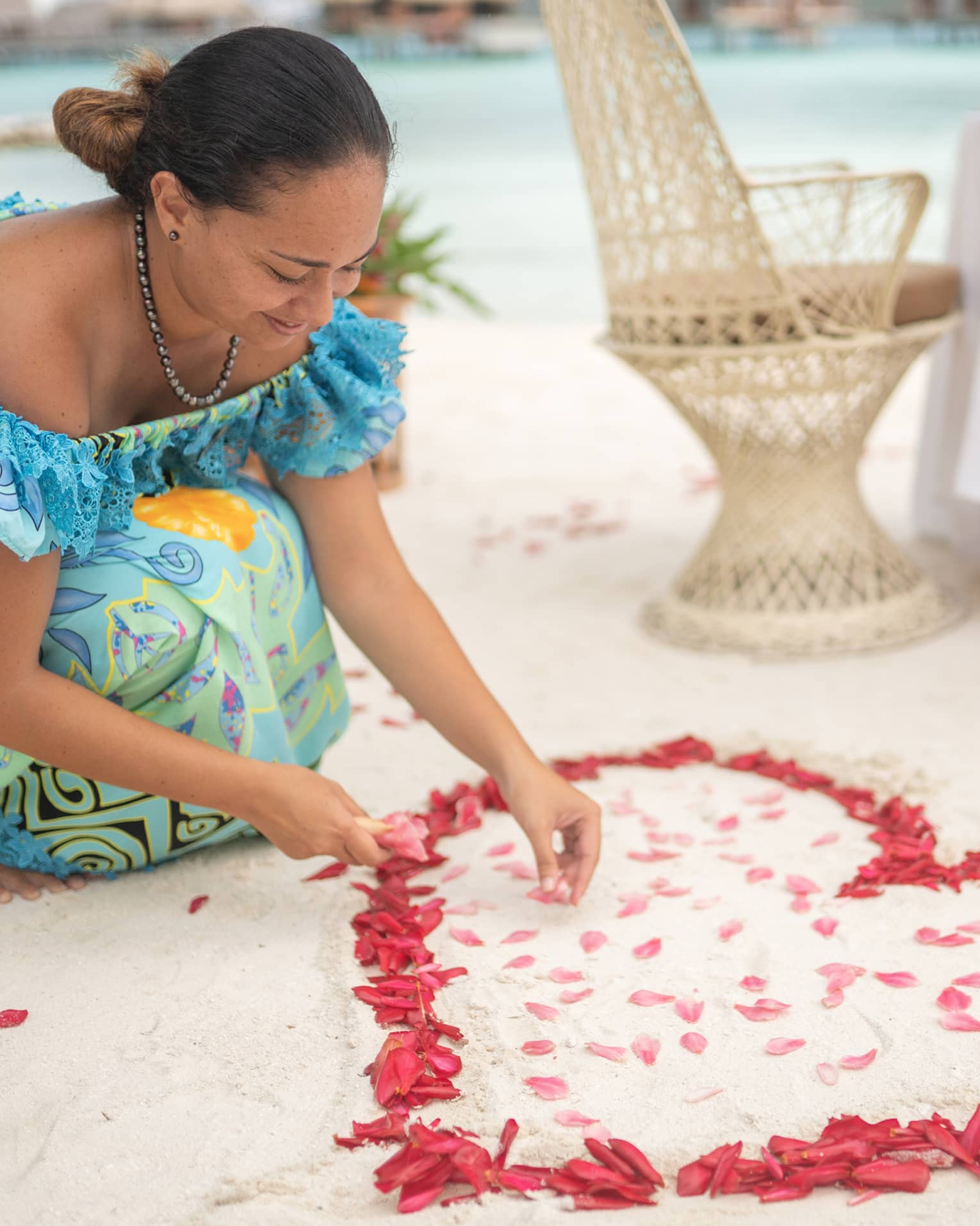 Woman arranges red rose petals into heart shape on sand beach