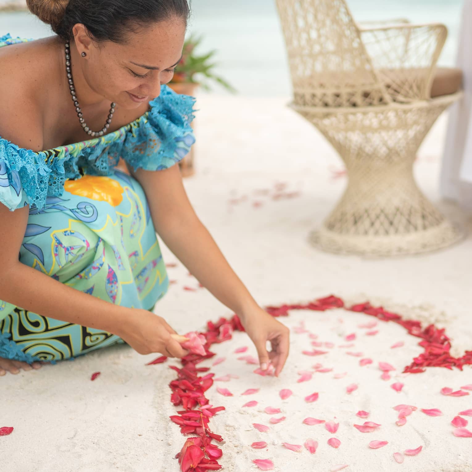 Woman arranges red rose petals into heart shape on sand beach