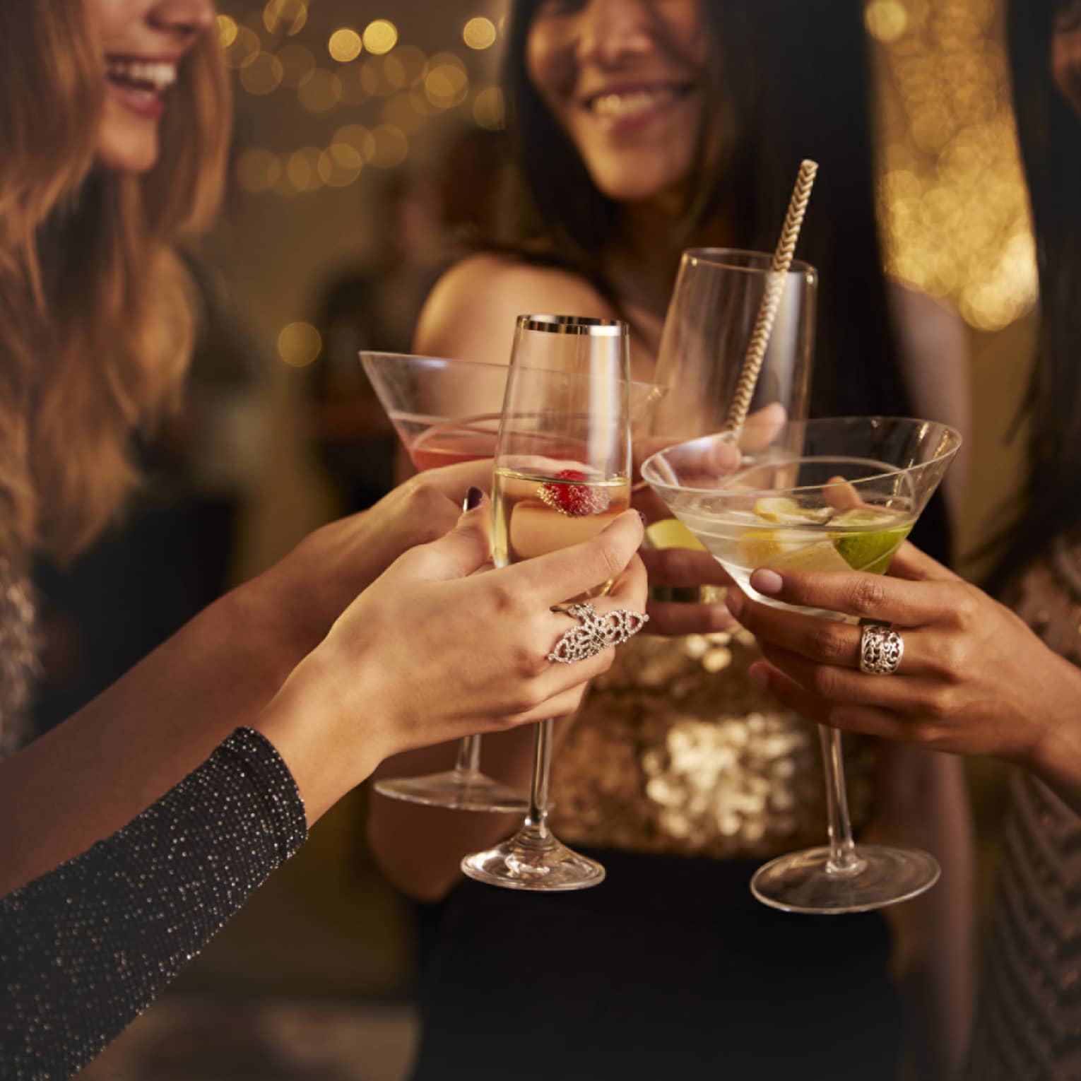 Four women in evening wear clink their cocktail glasses