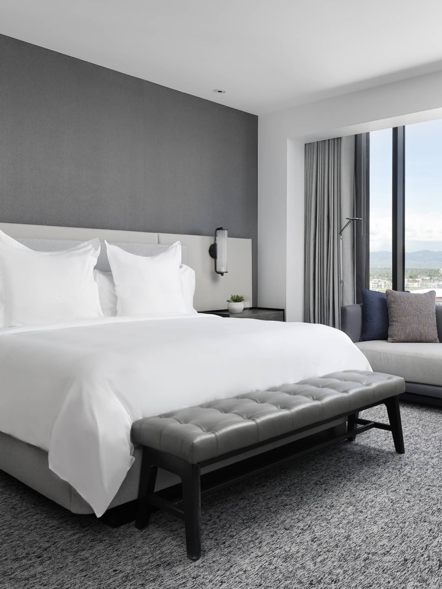 Hotel room bed, bench, small table and chaise by floor to ceiling window