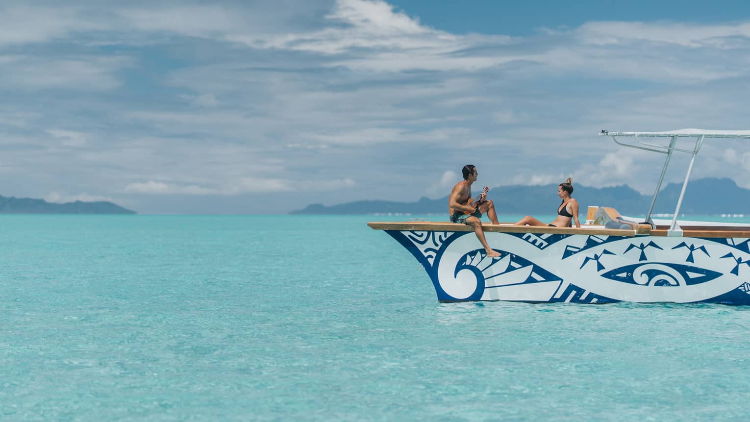 Man plays ukulele for woman on catamaran boat on lagoon