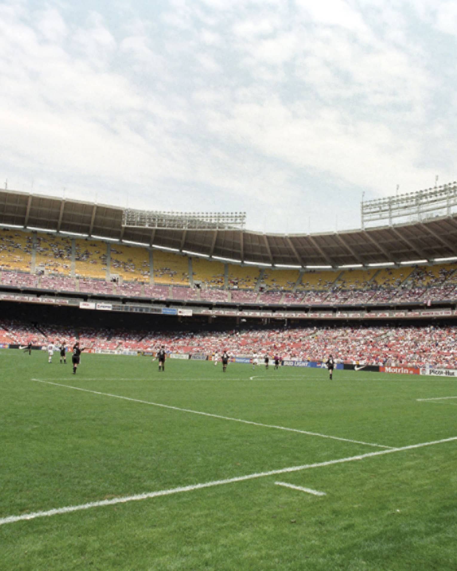 View across soccer field with players below crowds in stadium stands 