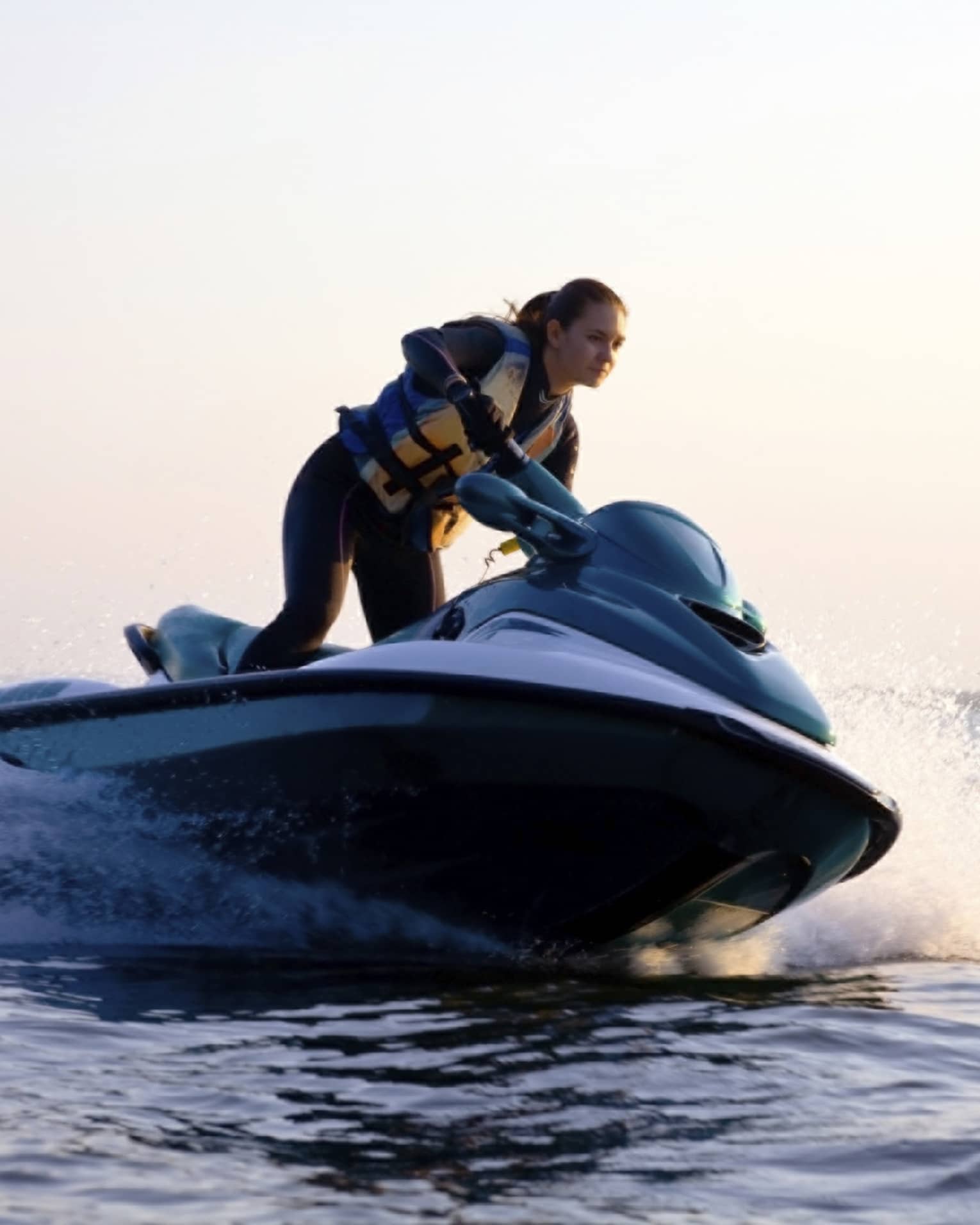 Woman wearing life jacket stands, steers jet ski on ocean at sunset