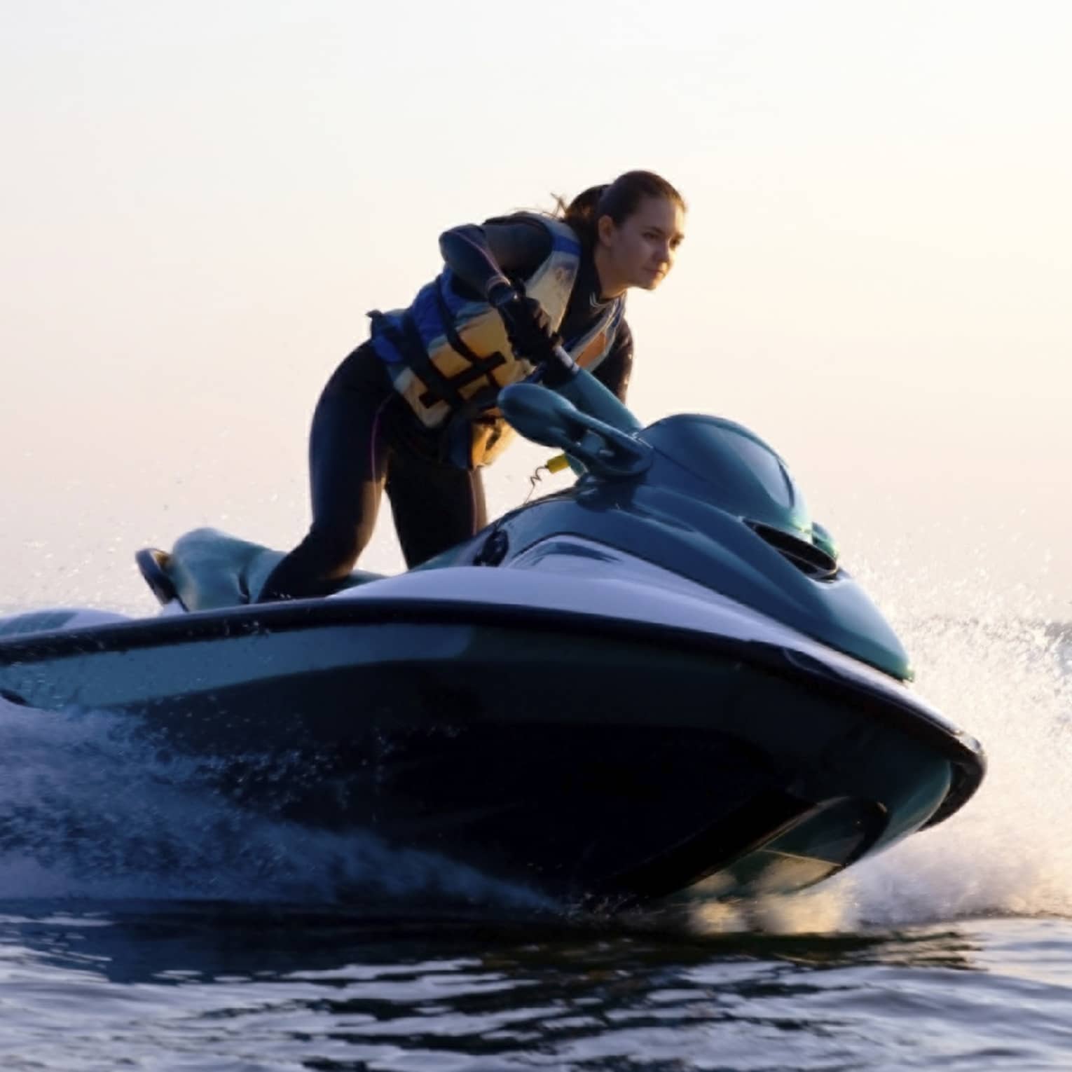 Woman wearing life jacket stands, steers jet ski on ocean at sunset