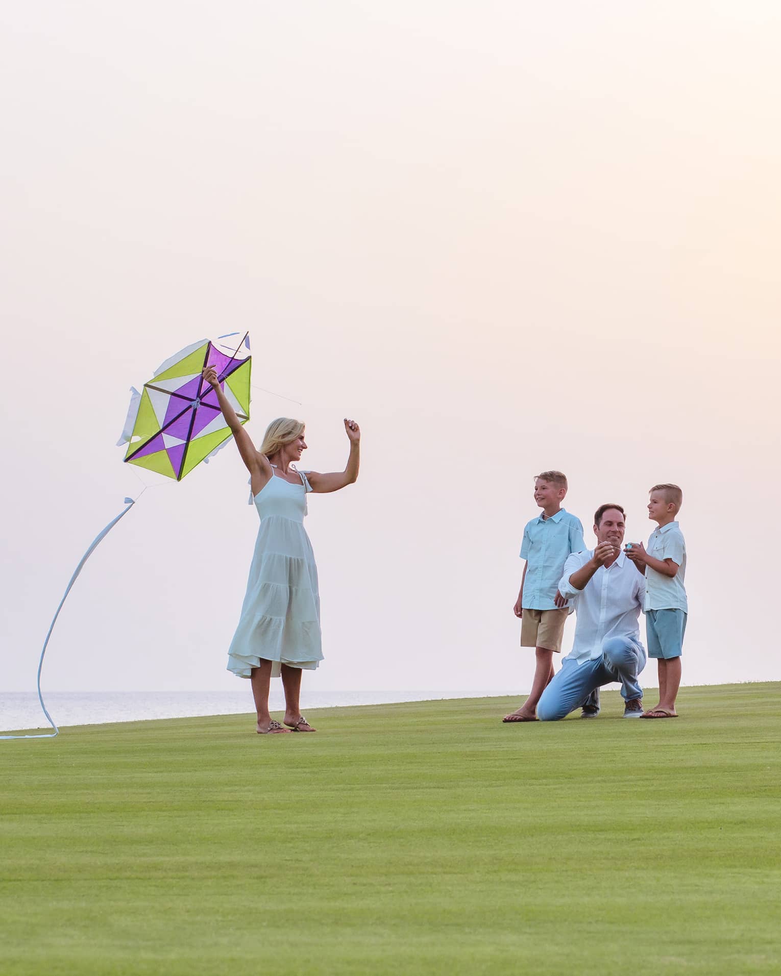 A family about to fly a kite while resting on green grass.
