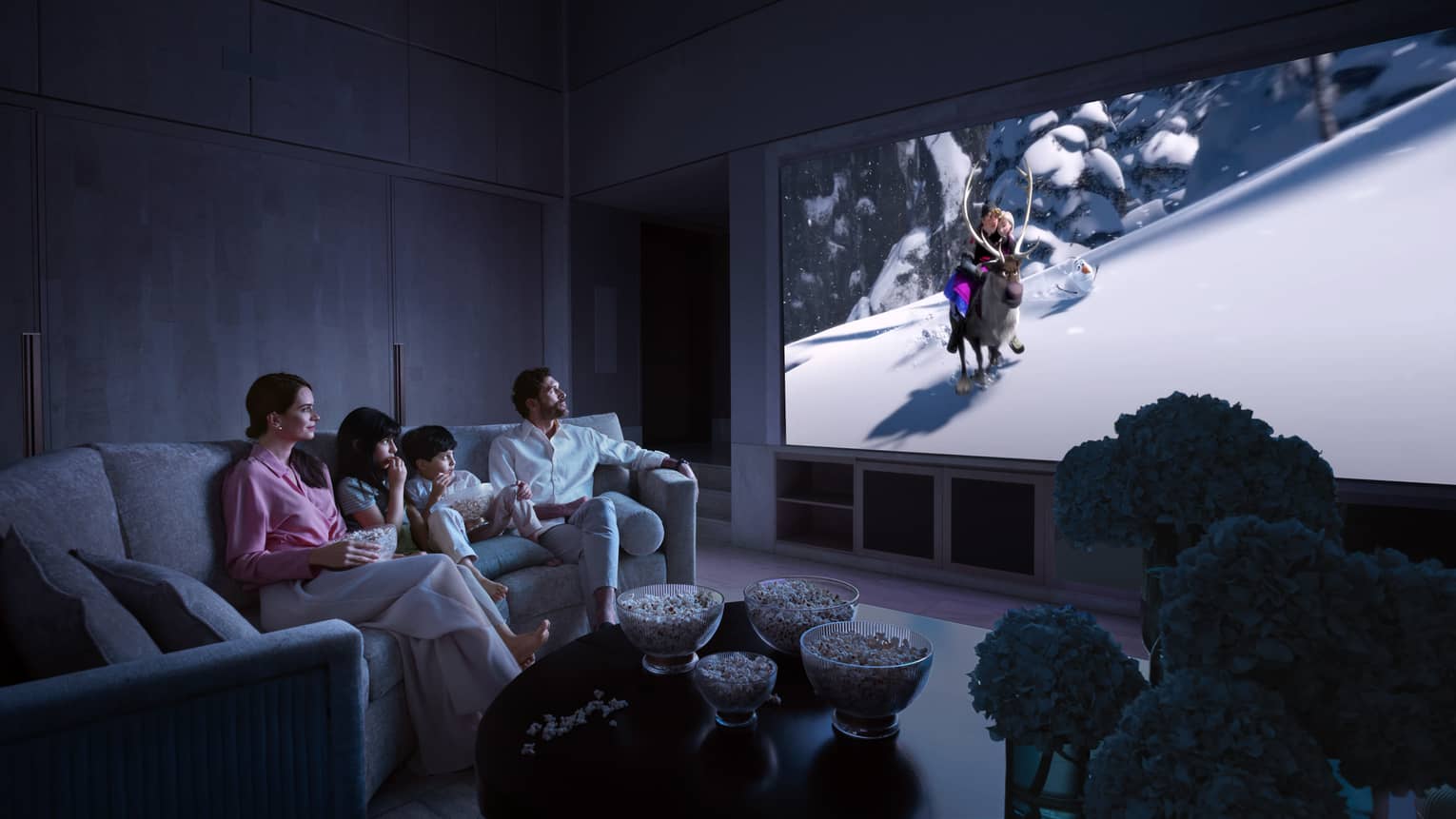 Family of four watches a film during a suite movie night, bowls of popcorn on a table in front of them