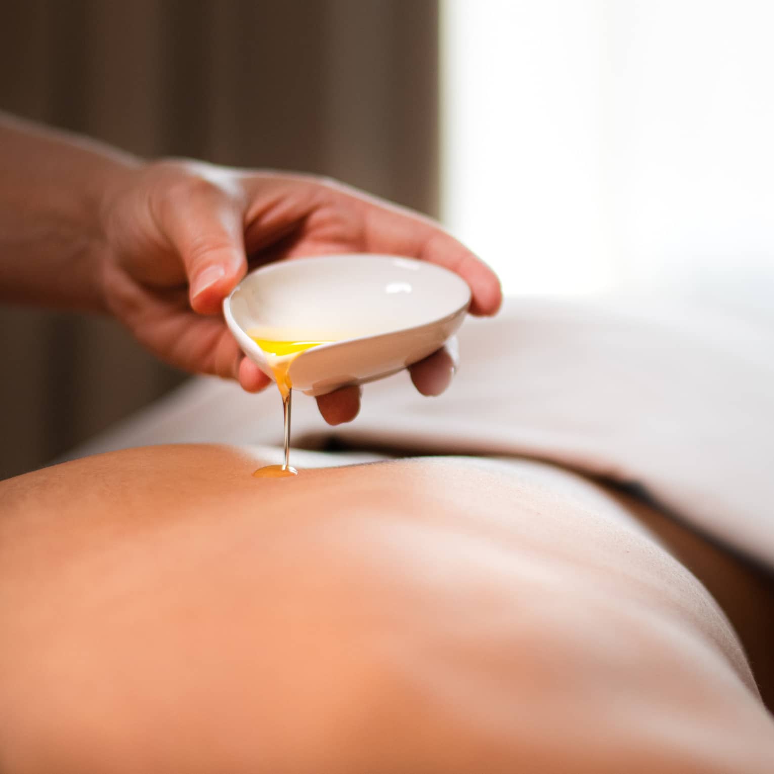 A spa staff member pouring liquid onto a woman?s back.