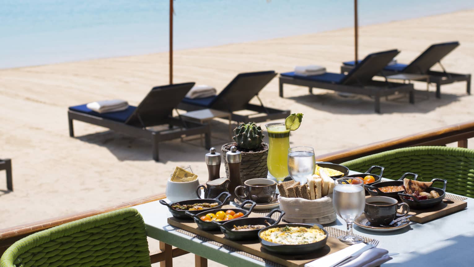 Patio dining table with breakfast items in front of sunny beach, lounge chairs