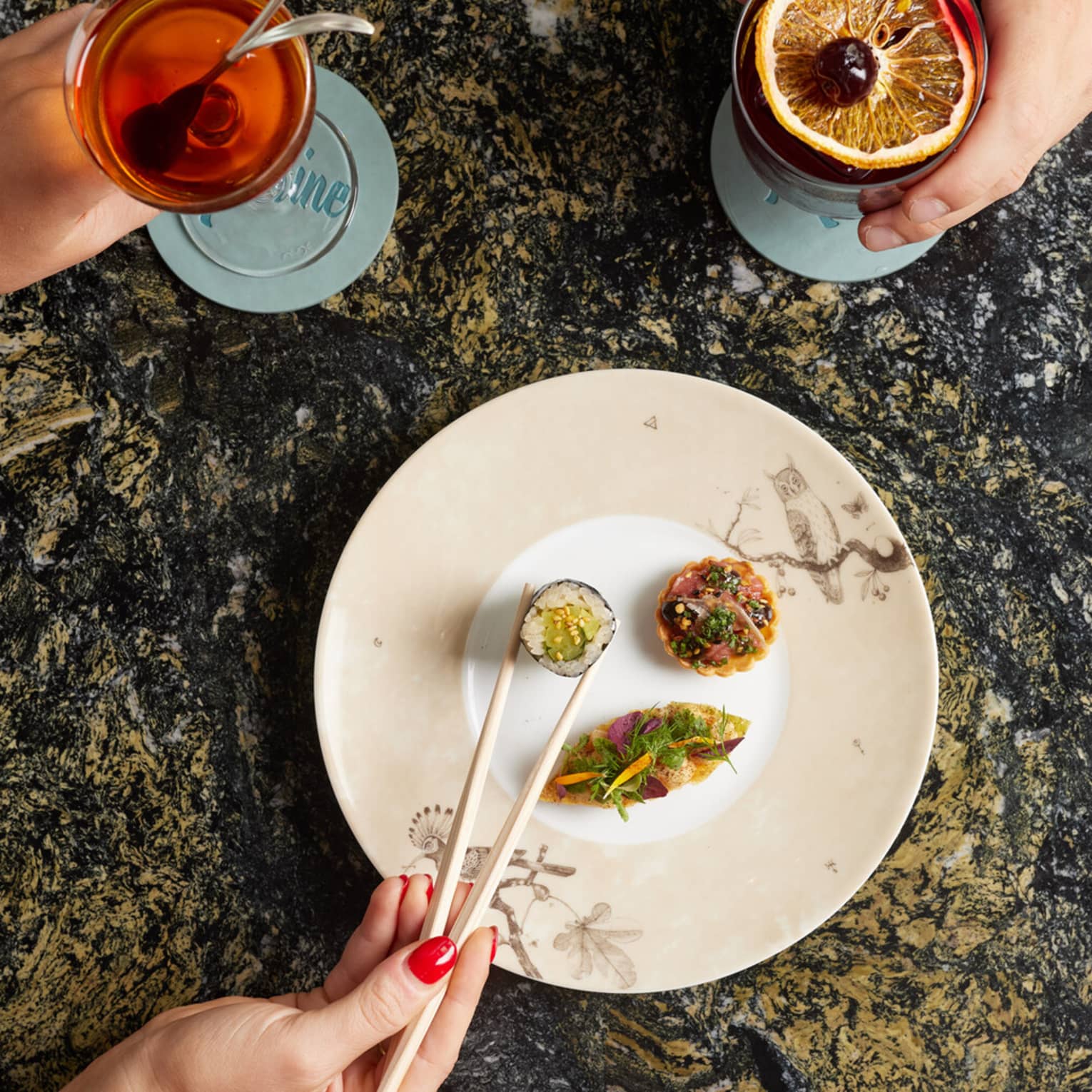 Left hand holding cocktail and right hand picking up sushi with chopsticks