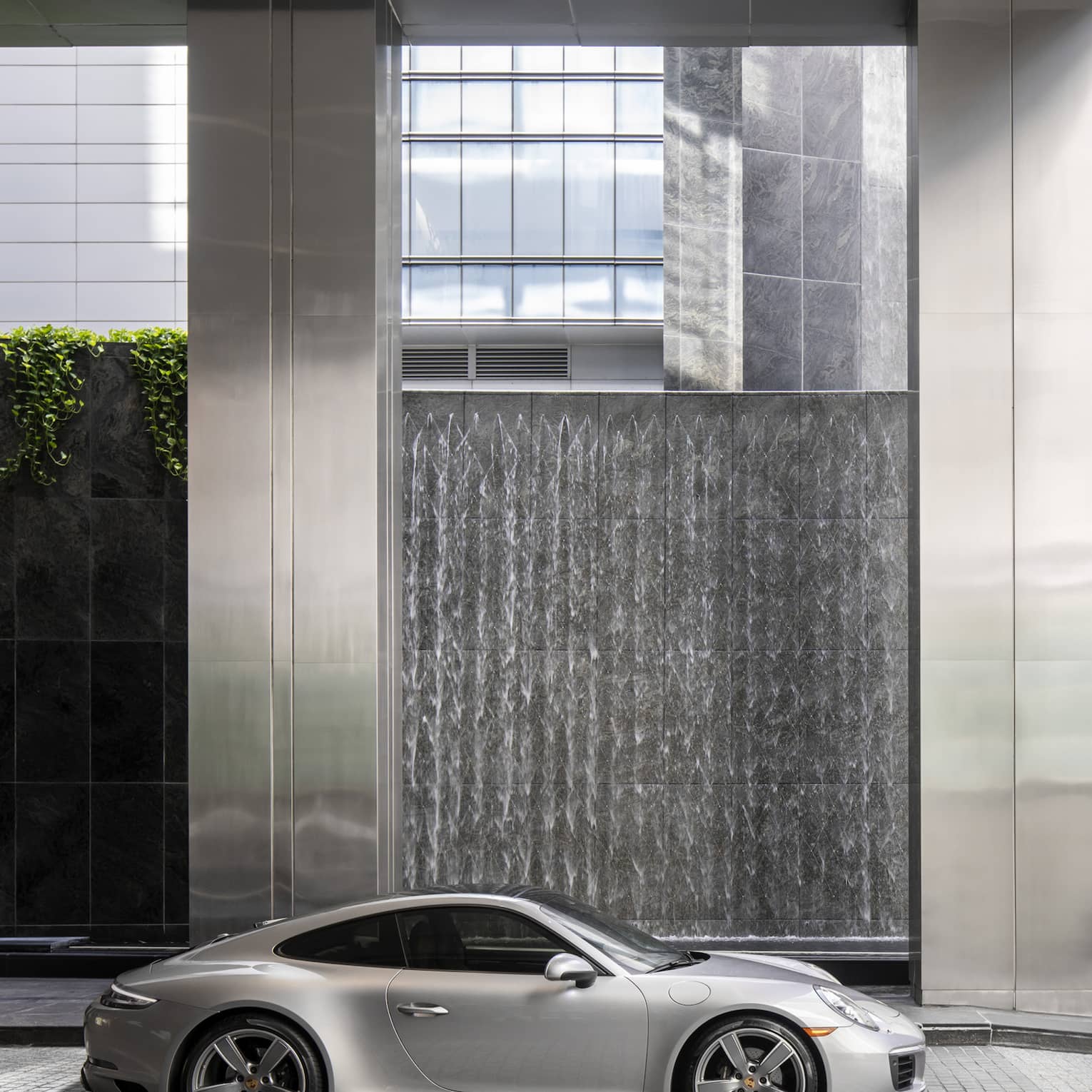 Silver Porsche sportscar parked in a modern structure with a high ceiling and gleaming stainless-steel columns.