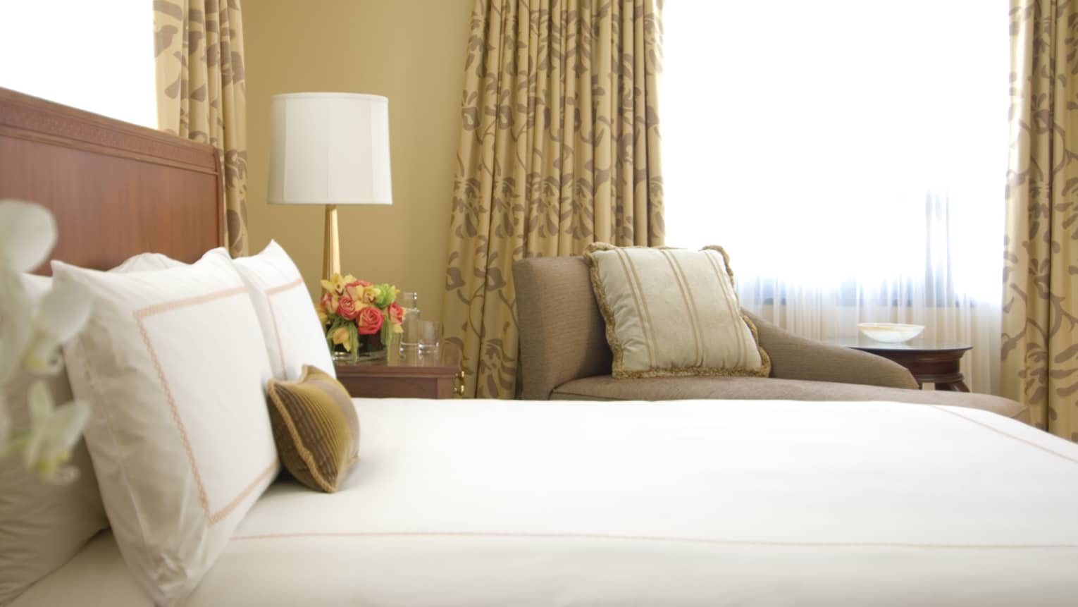 Deluxe City-View Room white orchids, side of bed, pillows against headboard, armchair, window in background