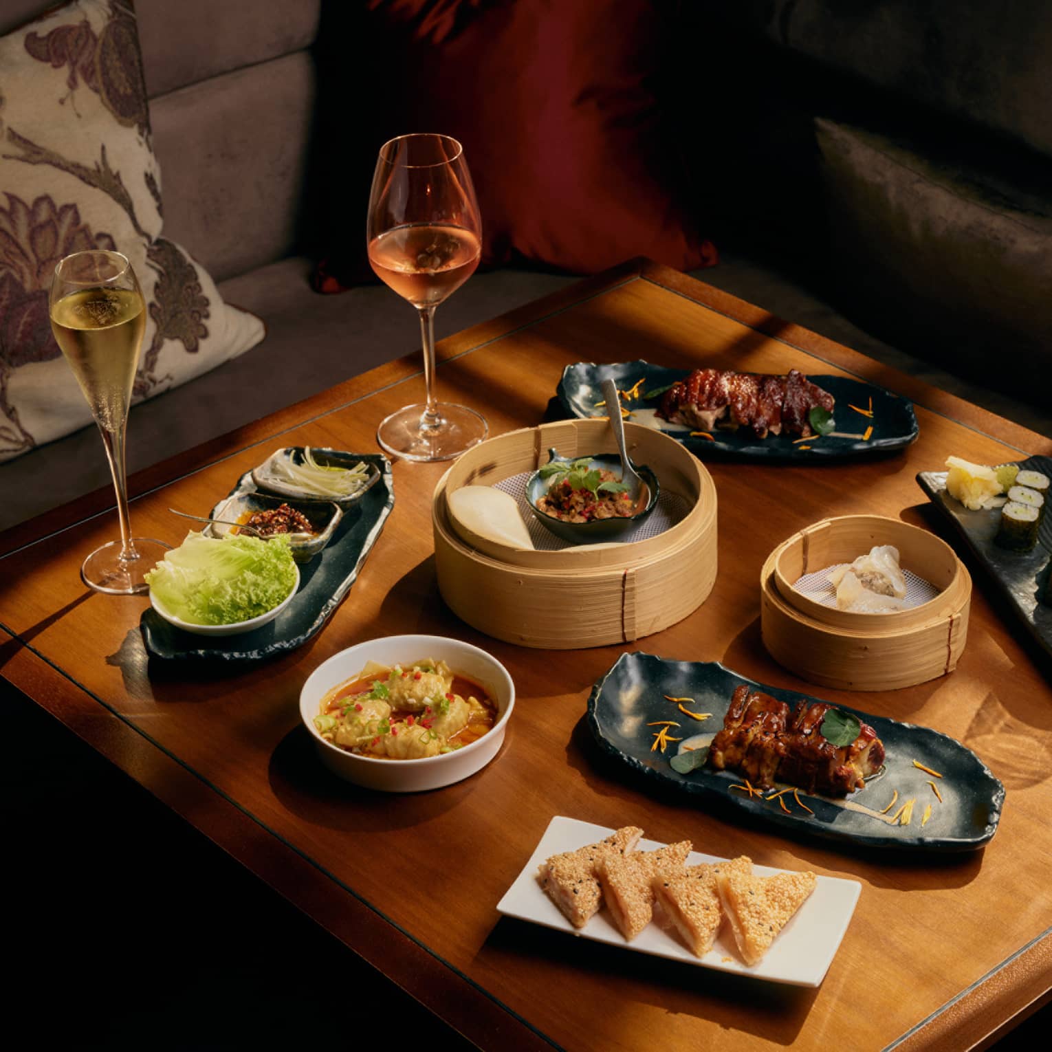 Assorted dim sum and glasses of wine on square wooden table