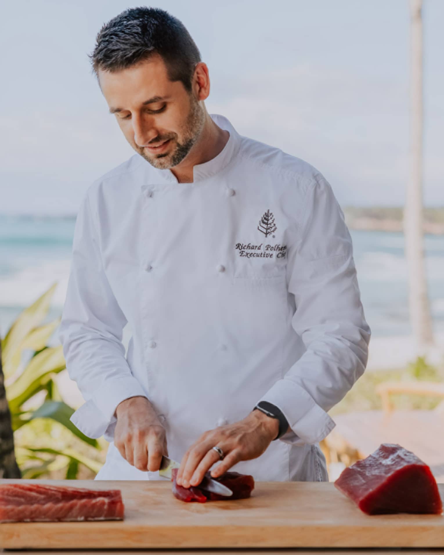 Male chef slices raw tuna on cutting board, beach in background